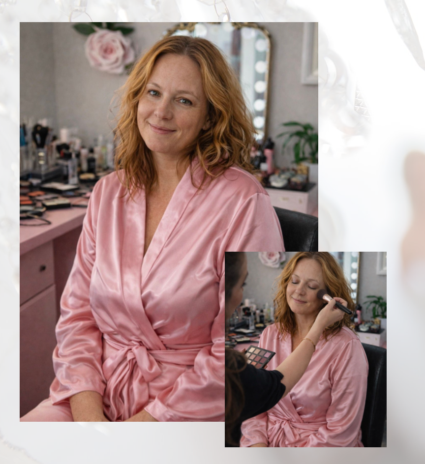 A woman in a pink satin robe sits at a vanity mirror while receiving professional makeup application in a studio.