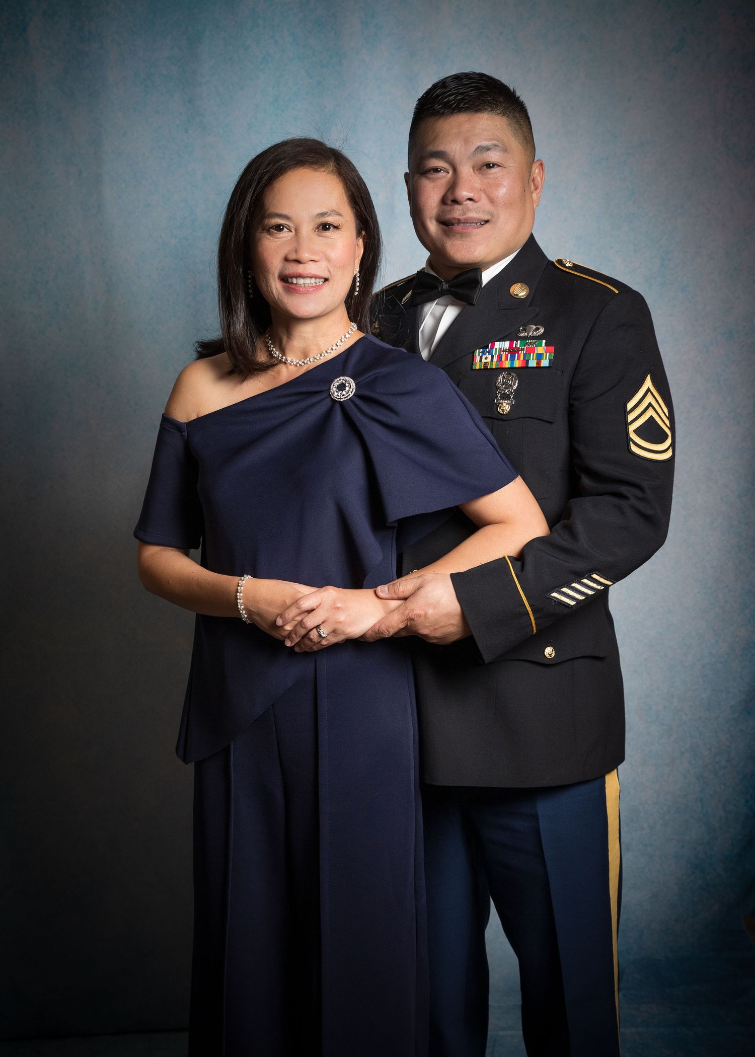 Couple posing at military formal, man in Army dress uniform with medals and woman in navy off-shoulder gown.