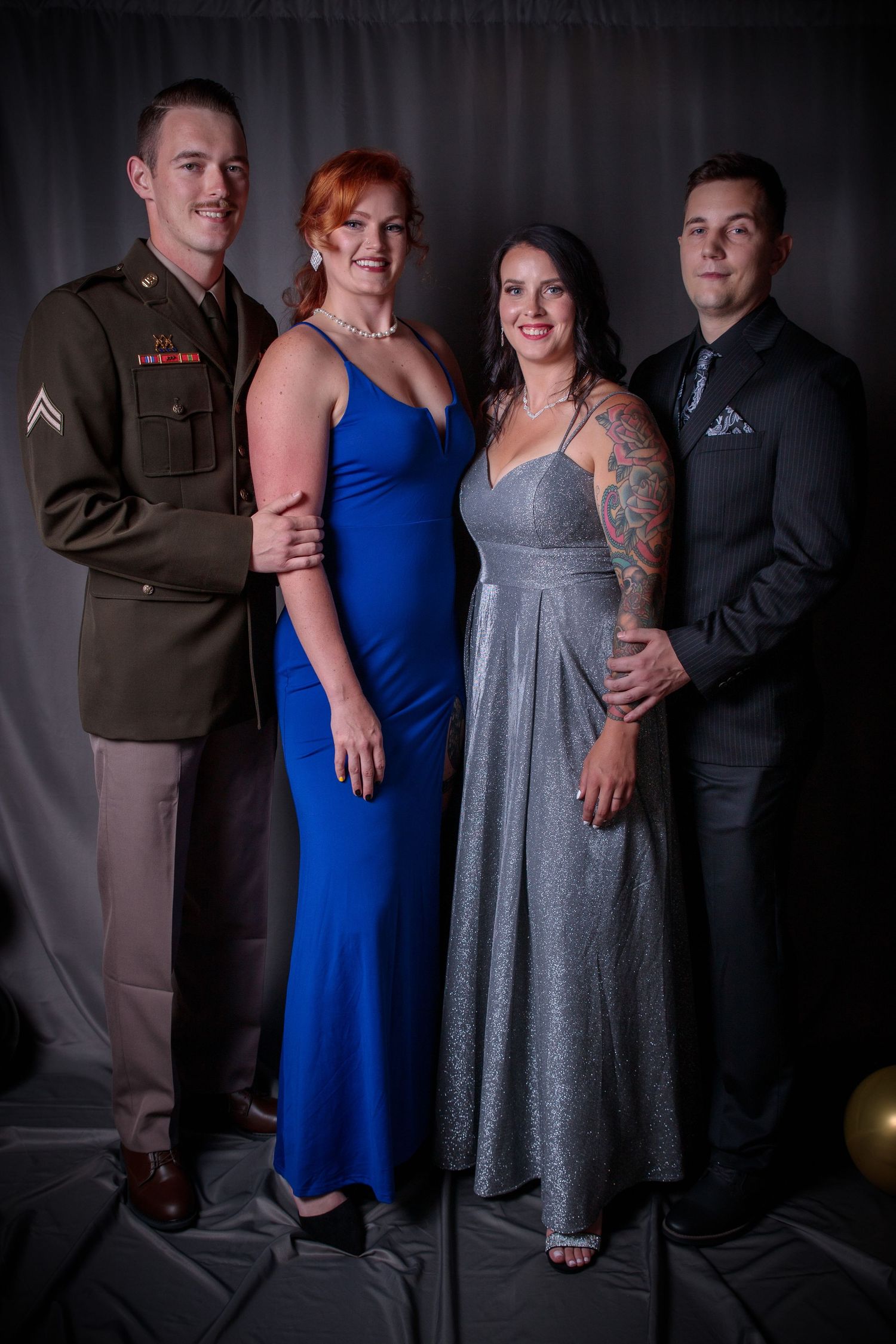 Two military couples posing together at formal event, one man in Army uniform with dates in blue and silver gowns.
