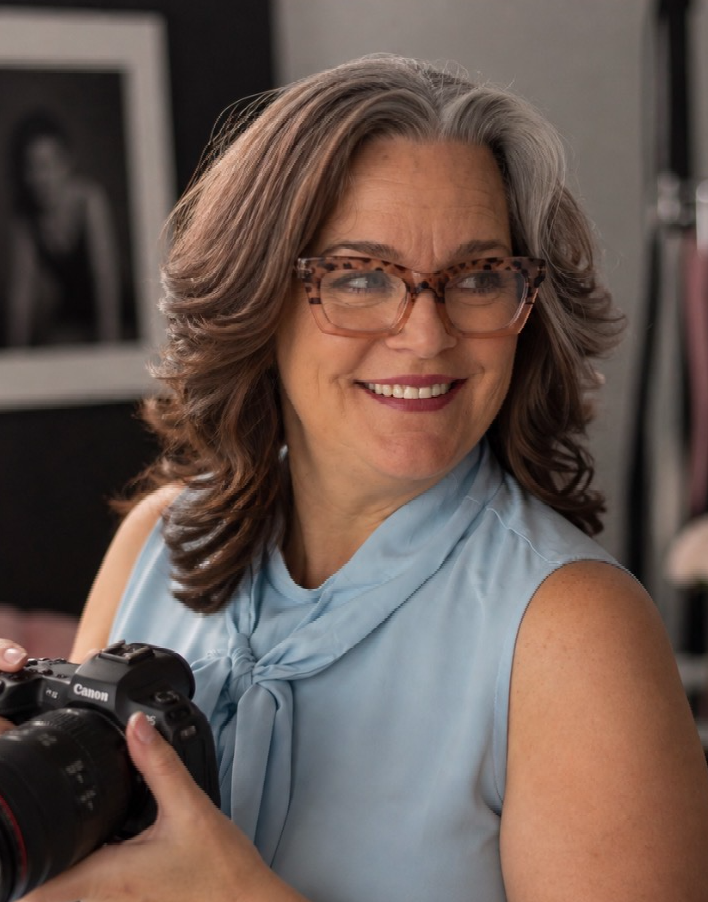 Professional female photographer smiling and holding a Canon camera in a photography studio.