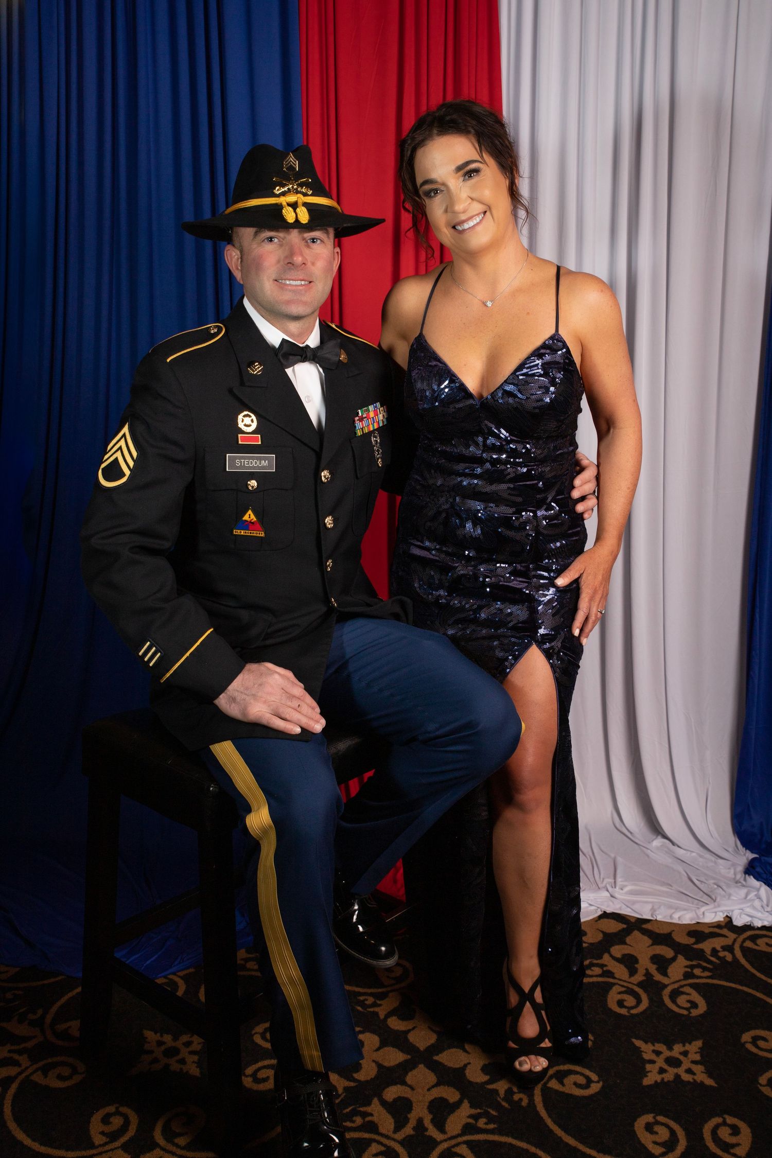 Army soldier in dress uniform and woman in sequin gown posing at a military ball.