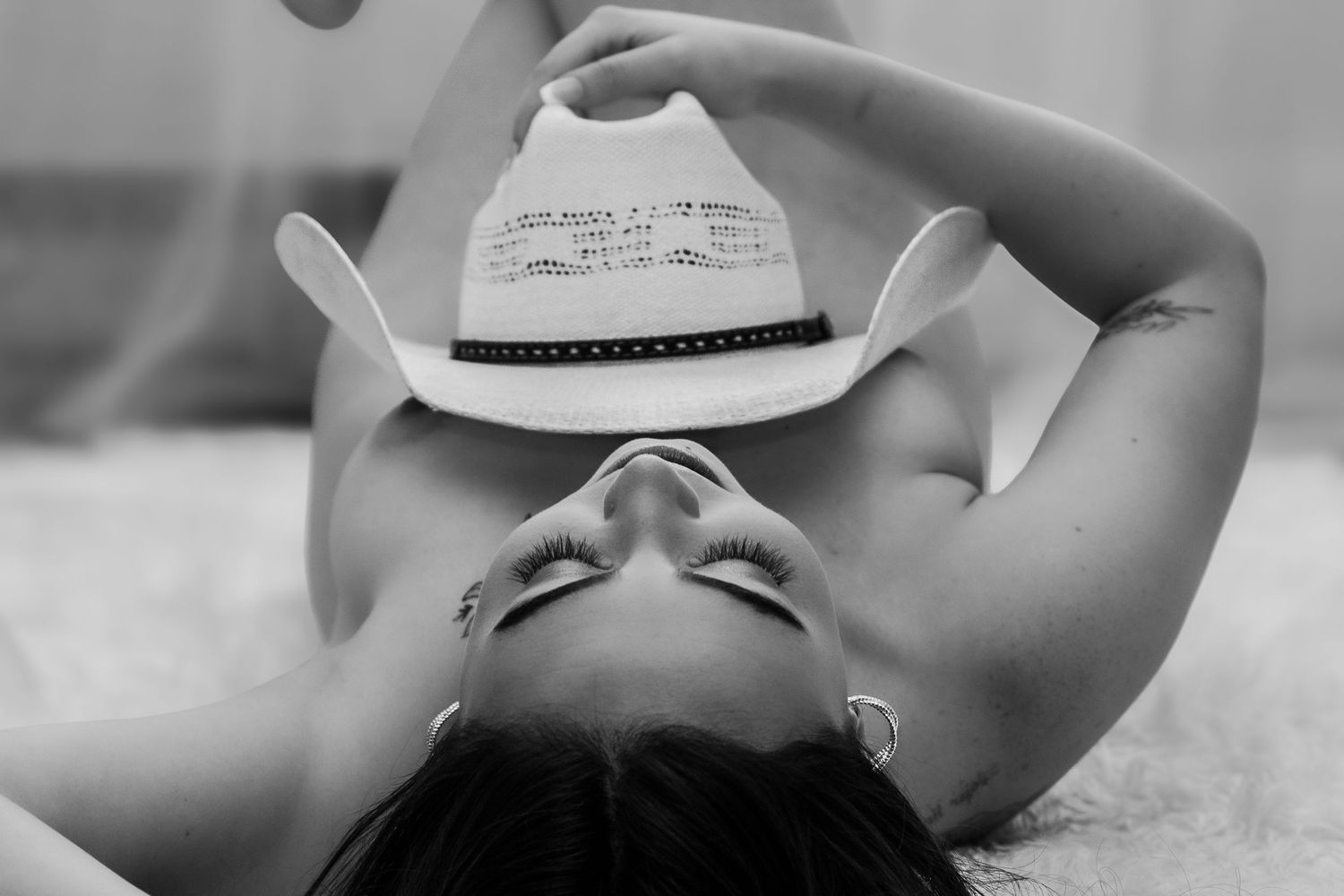 Black and white photo of a woman lying back holding a white cowboy hat over her face.