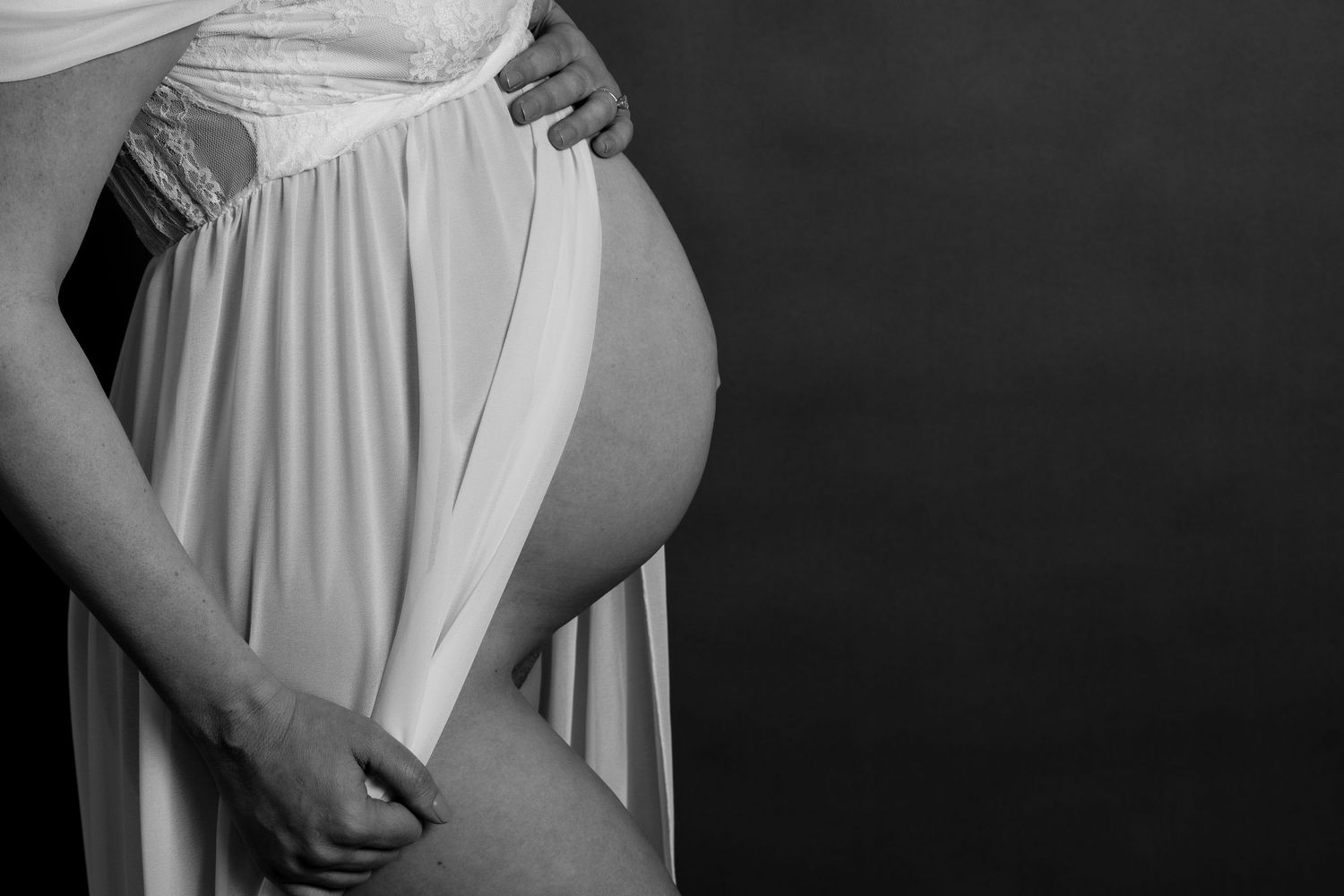 Black and white maternity photo of pregnant woman in white dress.