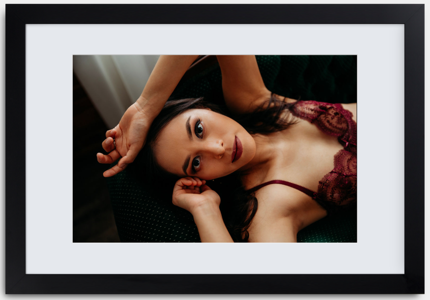 Woman in burgundy lace lingerie lying down, gazing up in a moody framed boudoir portrait.