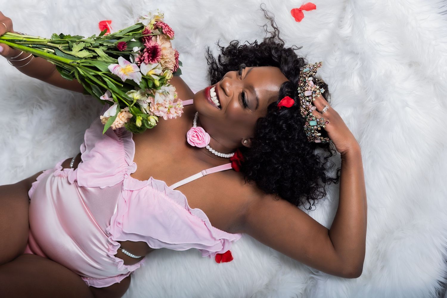 Smiling woman lying on fur with pink flowers and floral crown.