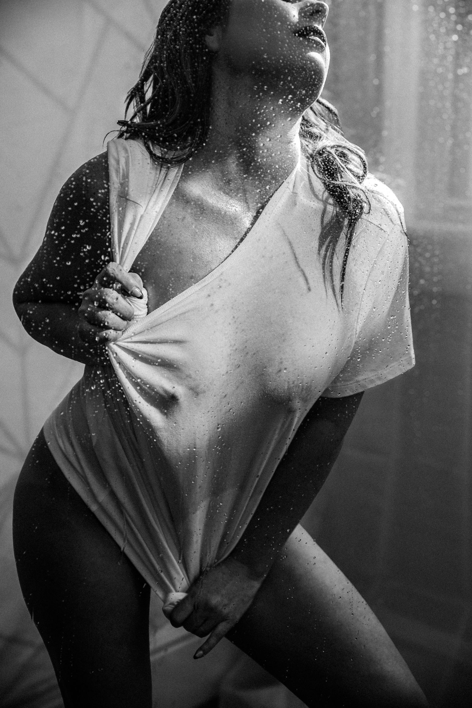 Black and white photo of a woman in a wet t-shirt posing dramatically with water droplets around her at a boudoir studio in Colorado Springs