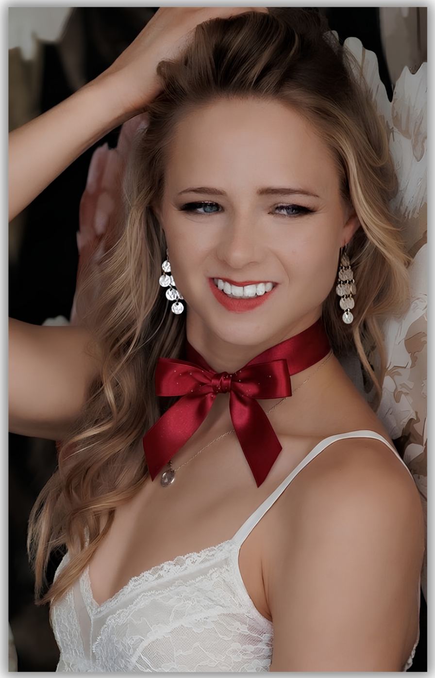 Young woman with blonde hair wearing a red satin bow choker, white lace top, and chandelier earrings, smiling.