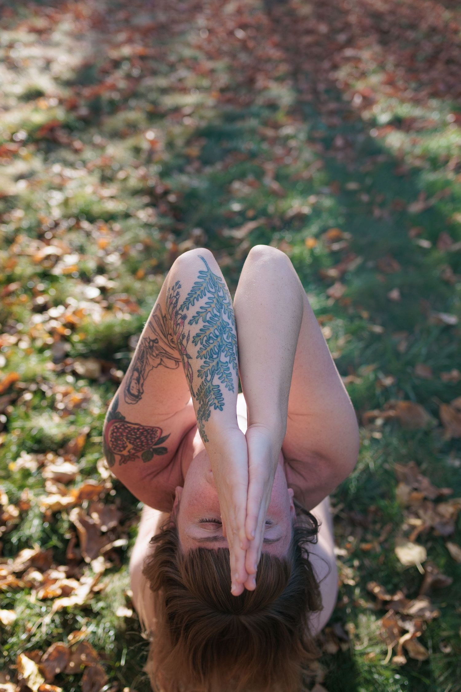 Woman with tattoos lying on autumn leaves in a park, legs raised in a yoga pose. Photography for yoga teacher in Boulder and Denver.