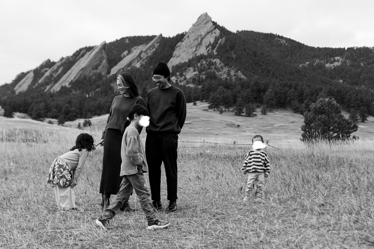 A family with three young children strolls through a meadow with the iconic Boulder Flatirons mountains behind them. Family photography.