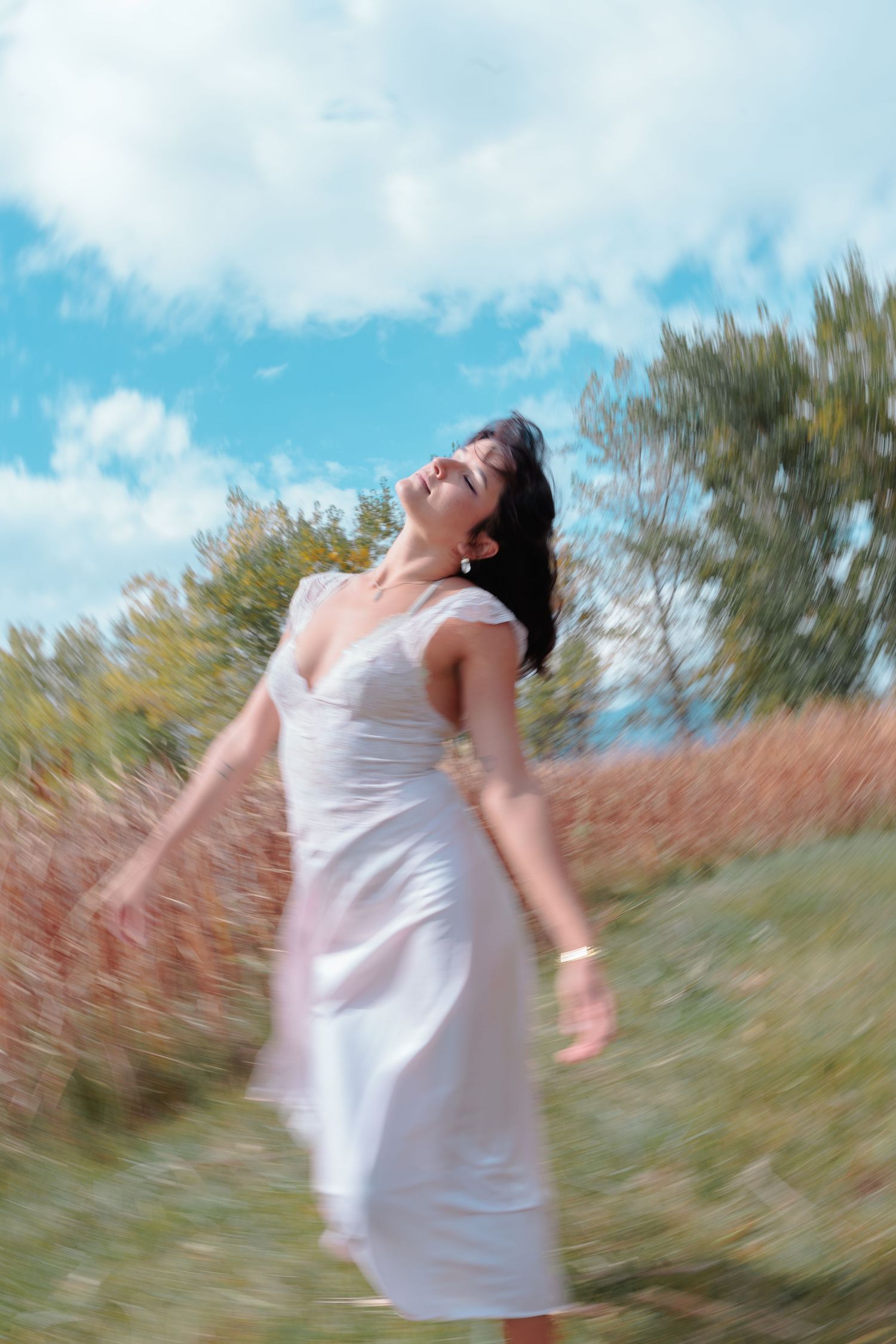 Woman in white dress spins joyfully in a field under a bright blue sky. Portrait session for Colorado musician.