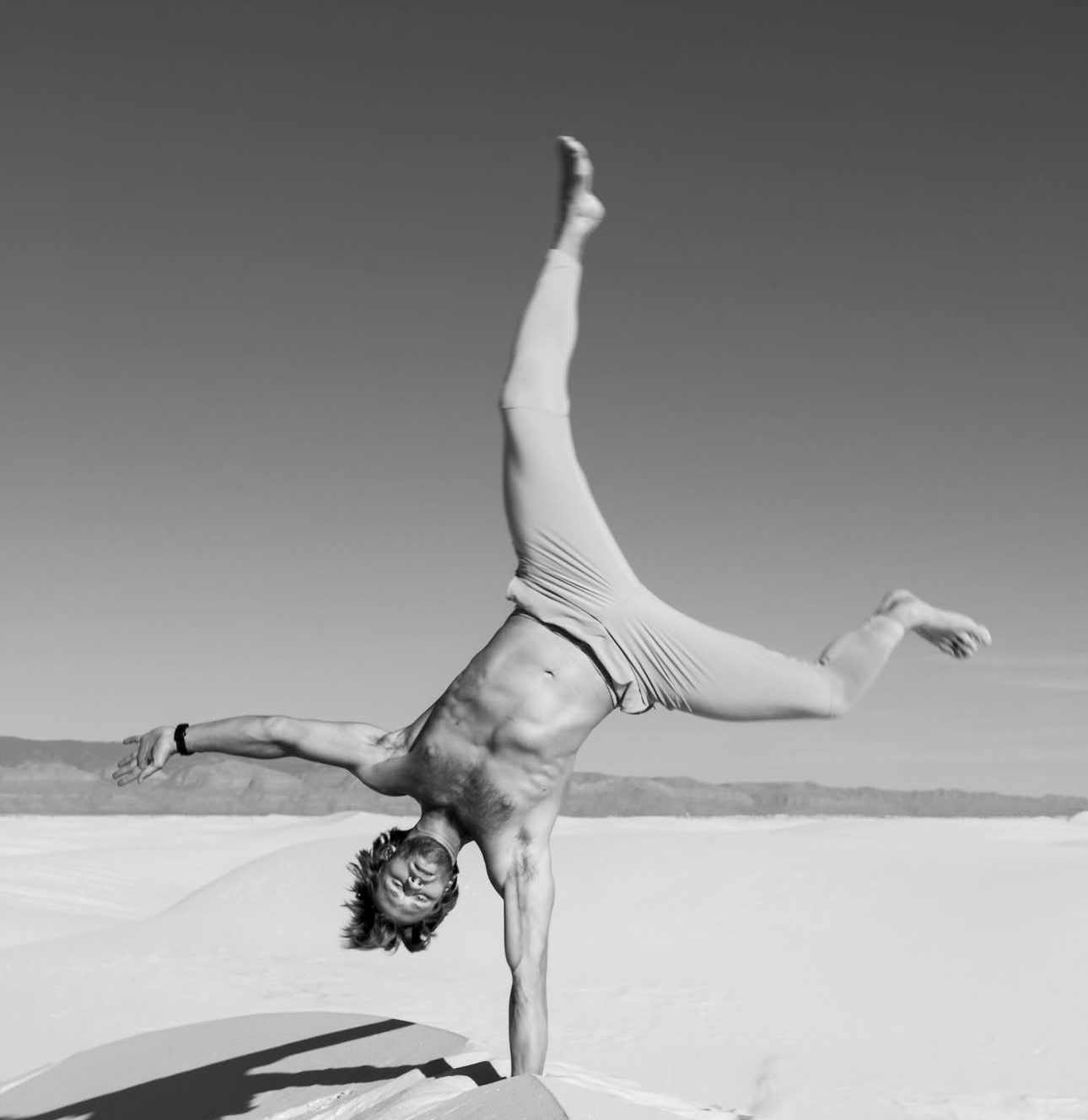 A muscular person performs a one-handed cartwheel on white sand flats in a black and white outdoor photo. Portrait photography New Mexico.