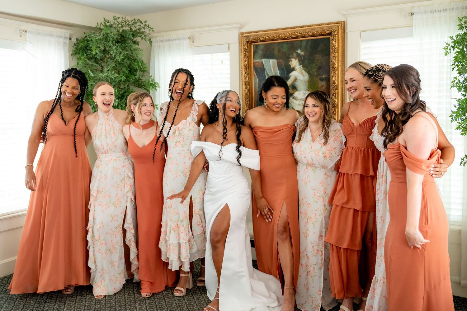 Joyful bride in white gown celebrating with bridesmaids in rust orange dresses indoors. Photography for wedding ceremony in Colorado.