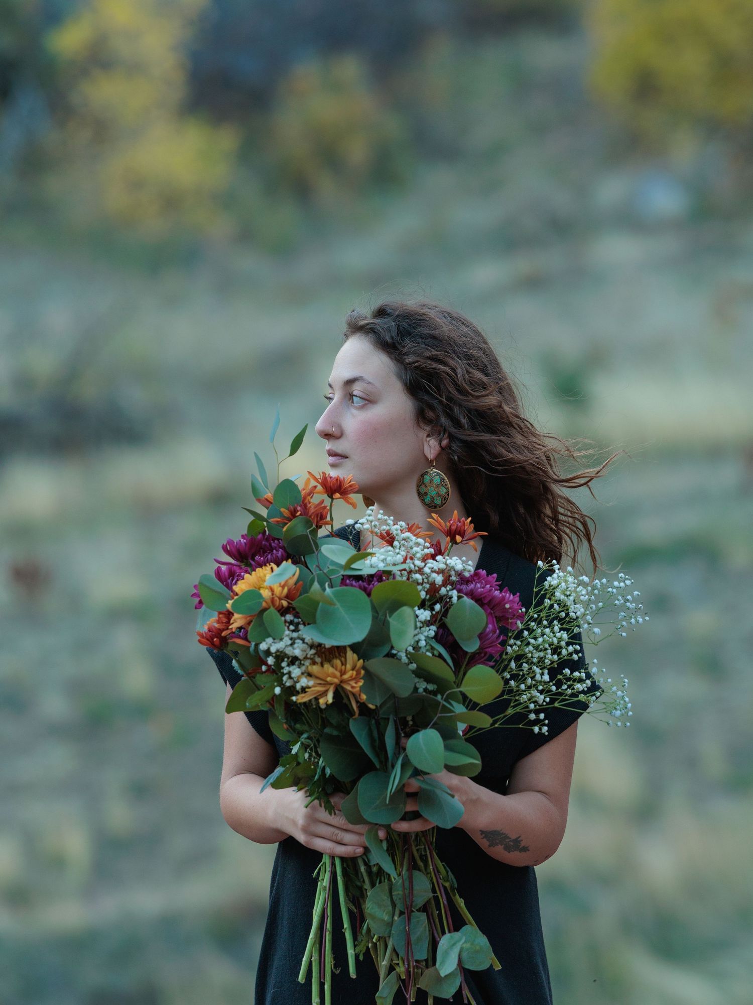 Woman holds a bouquet of flowers with hill behind her. Denver holistic energy work brand photographer.