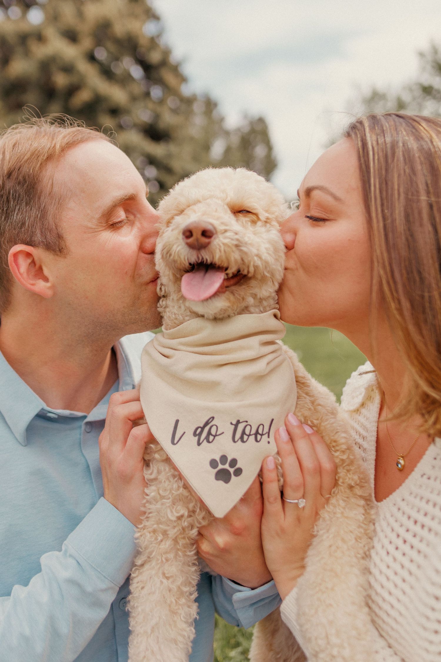Engaged couple kissing their fluffy goldendoodle wearing an I do too bandana. Engagement photography for a Colorado couple in Denver.