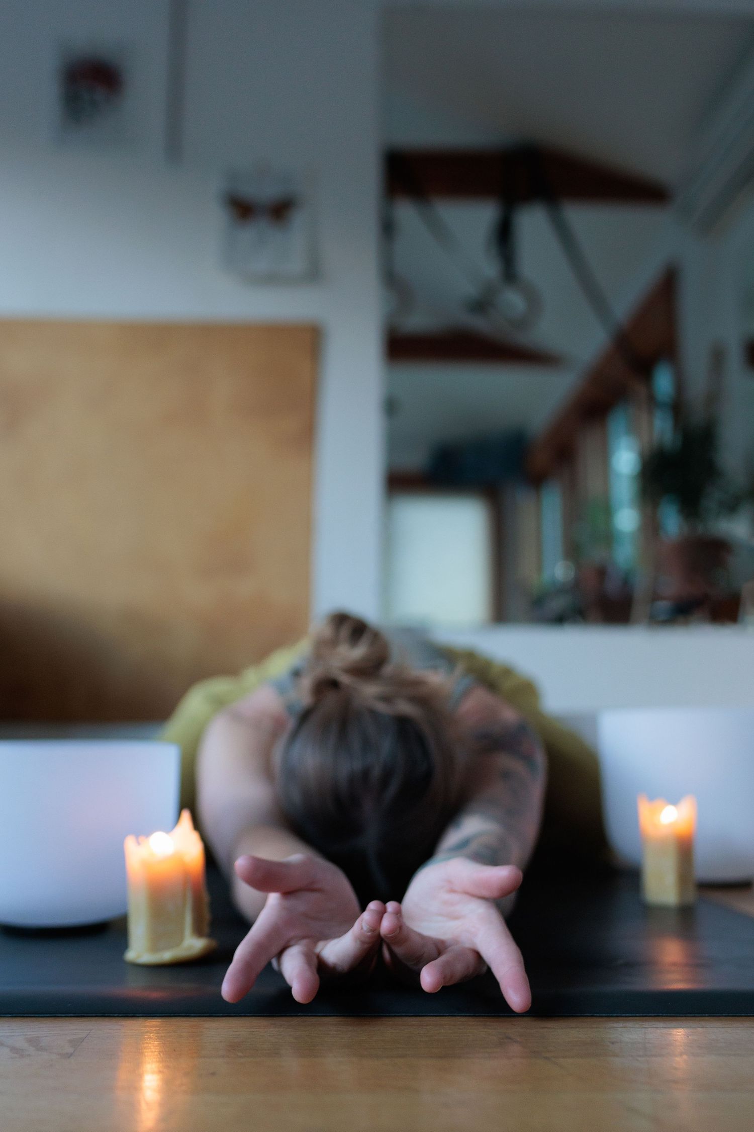 Woman in child's pose yoga position surrounded by glowing candles on a wooden floor. Energy work in Denver.