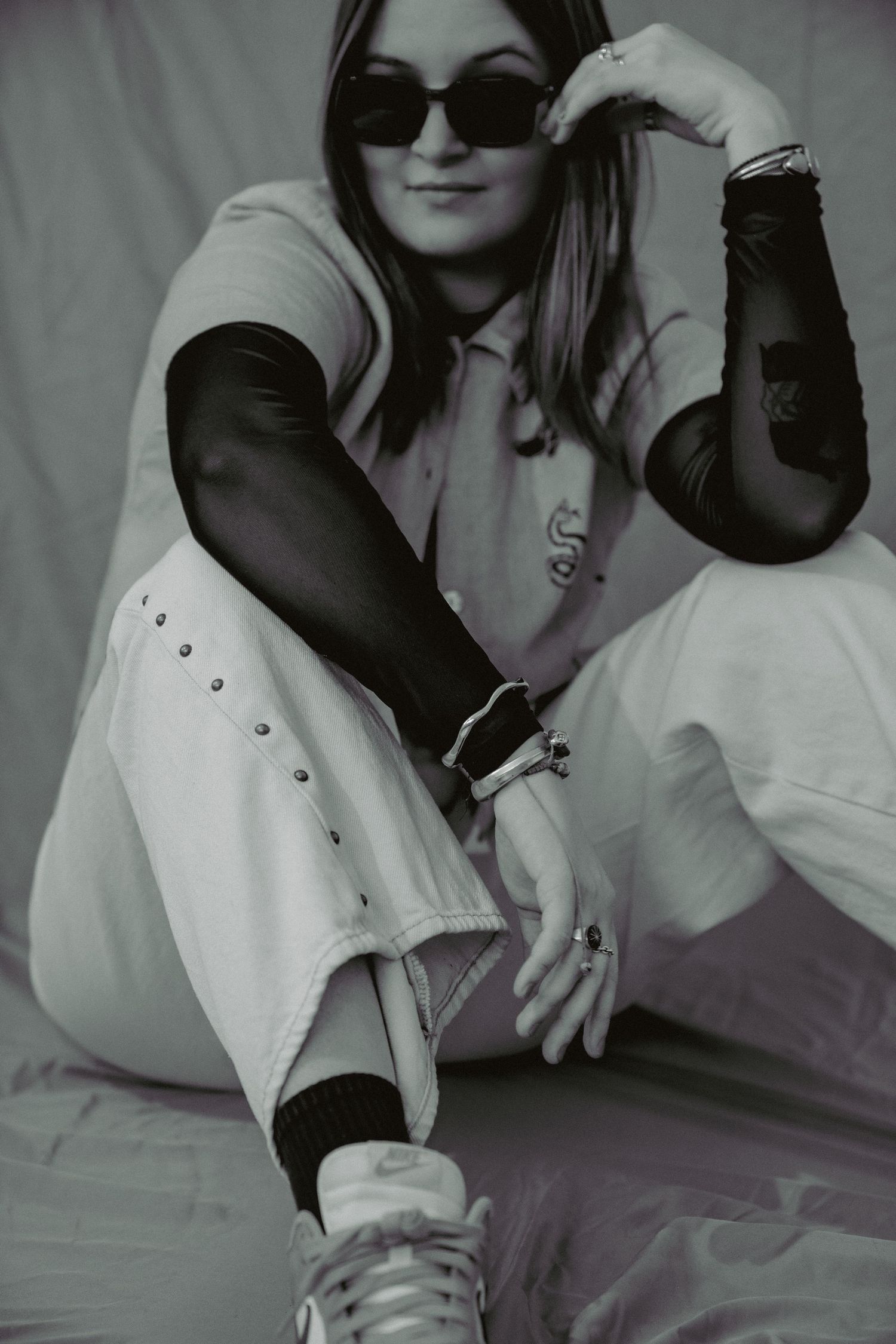 Black and white portrait of a woman in sunglasses and mesh sleeves sitting in a relaxed pose. Musician photography Denver.
