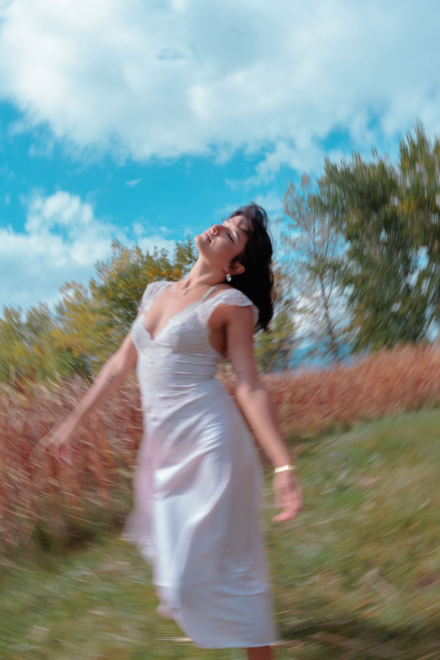 A peaceful woman in a white dress twirls in a sunny field, head tilted back under a blue sky. portrait photography for Denver musician.