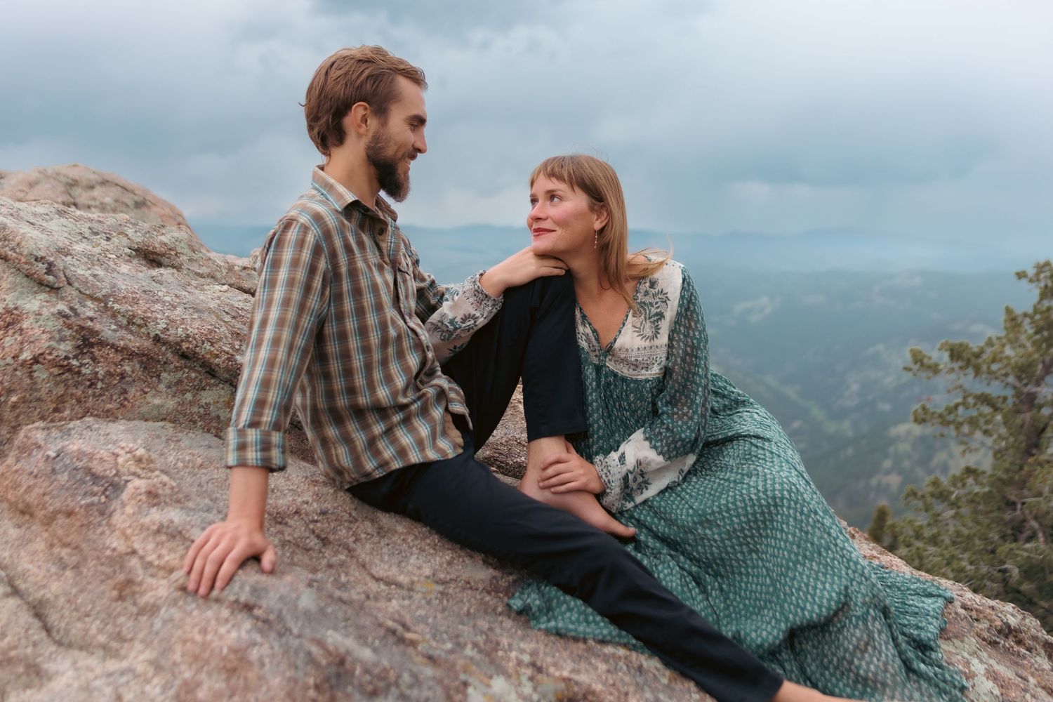 Couple sitting on mountain rocks sharing a tender moment with scenic valley views. Engagement photography for a Colorado couple.