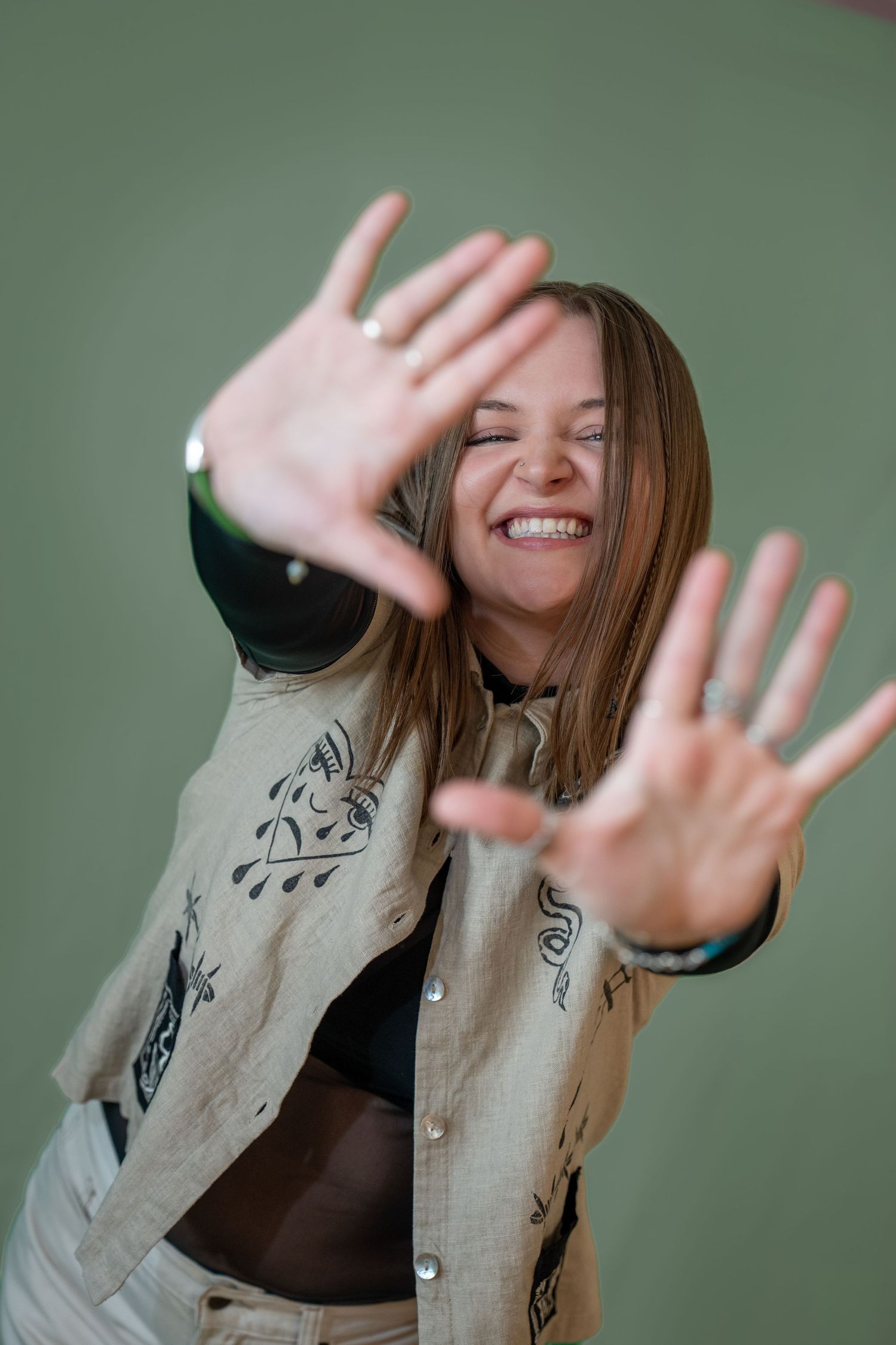 Smiling woman in embroidered jacket reaches hands toward camera against green background. Brand embodiment photos.