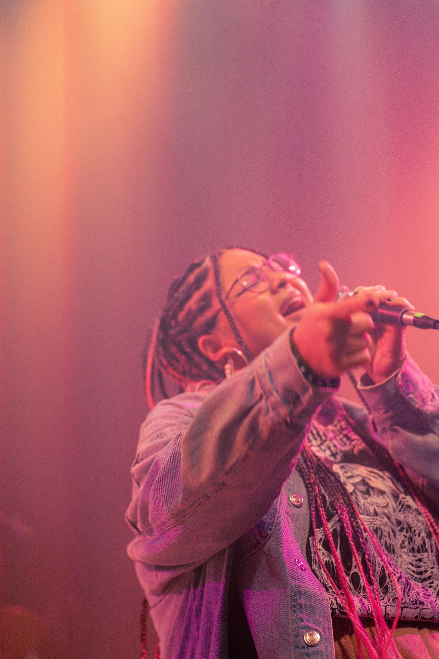 Female singer performing on stage under pink lights, holding microphone. Concert photography for Denver musicians.