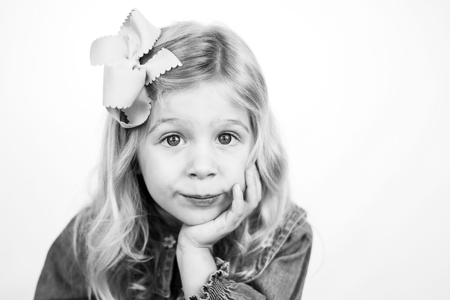 Black and white portrait of a young girl with long hair and a large bow, resting her chin on her hand.