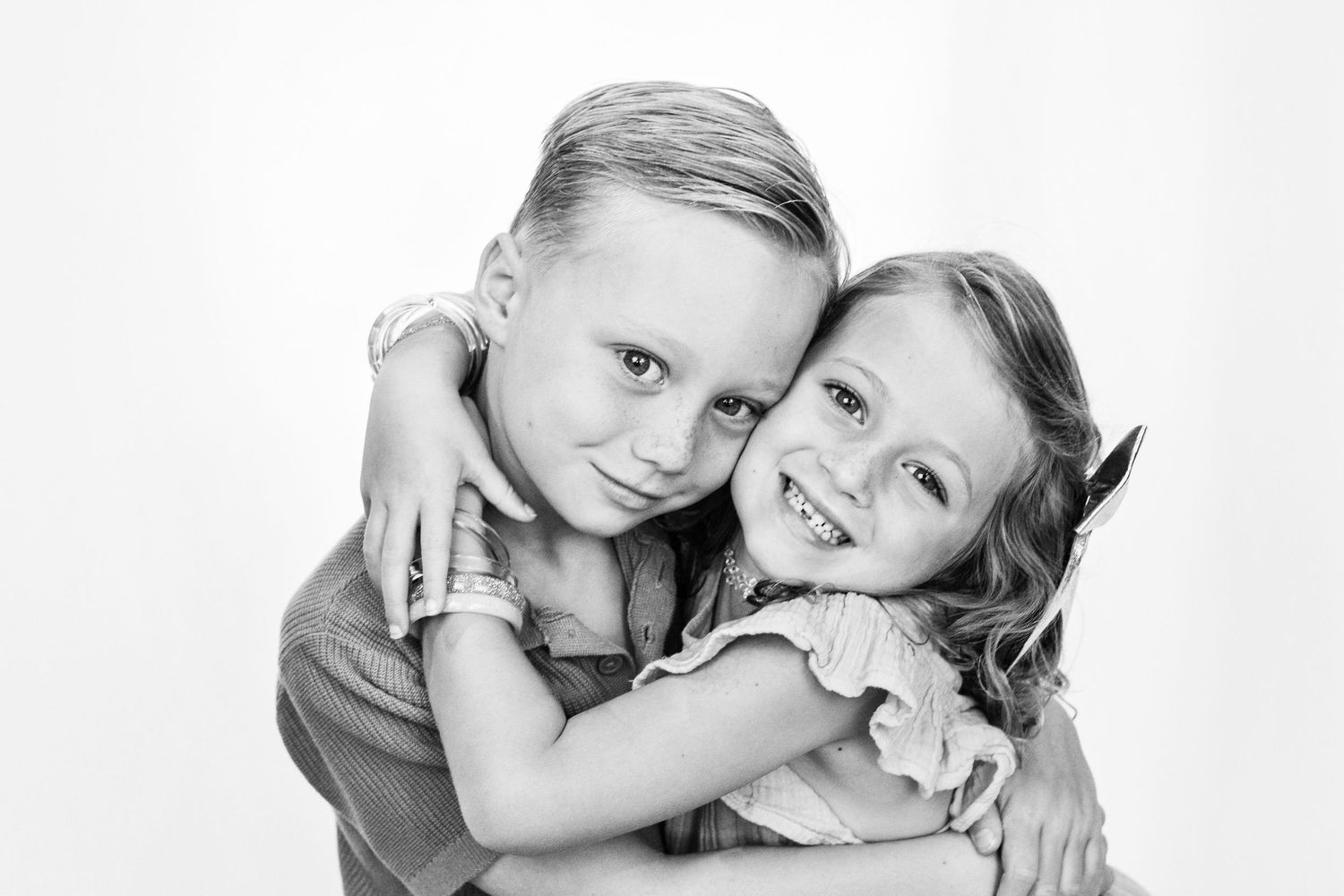 Two young siblings share a warm hug in a classic black and white studio portrait.