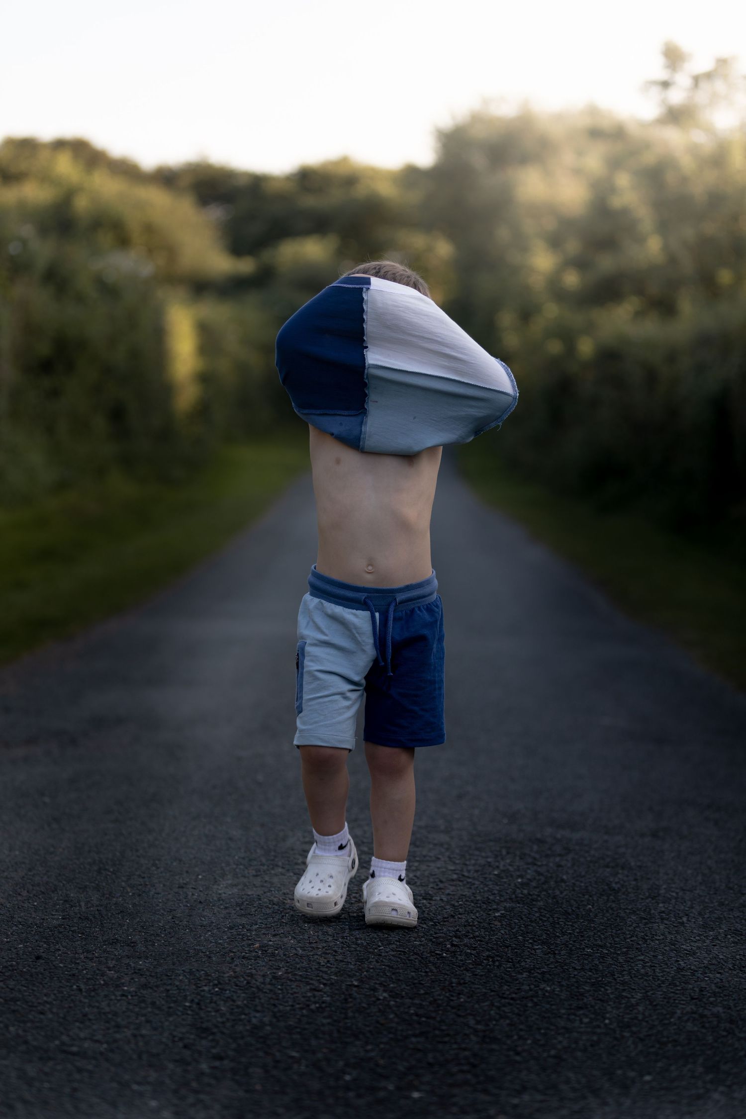 A young child pulls their blue and white shirt over their head while standing on a tree-lined road at sunset.

Blue Dolphin North Yorkshire