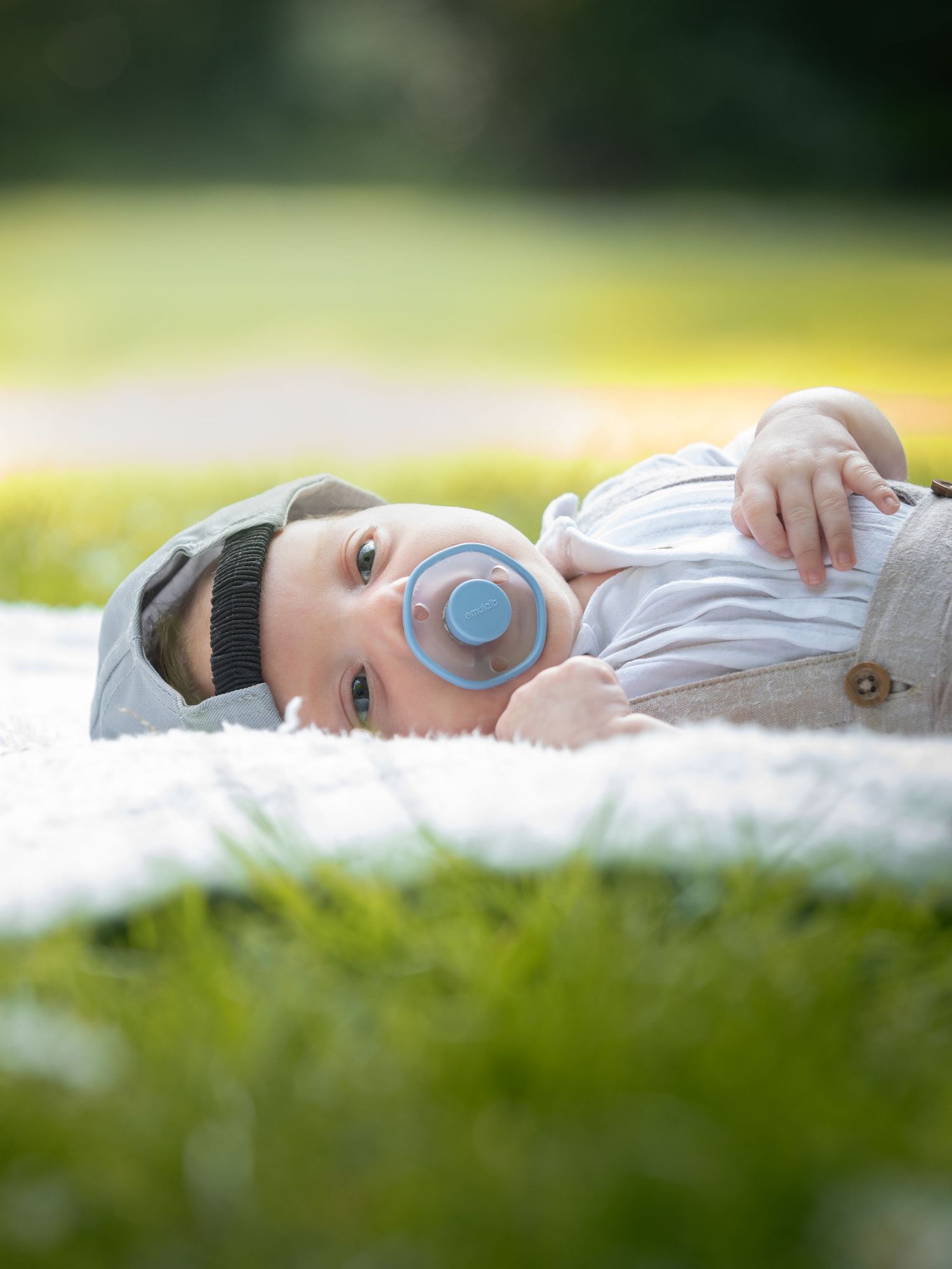Cute baby boy with blue pacifier lying on white blanket in green grass during outdoor photoshoot.

East Park Hull
