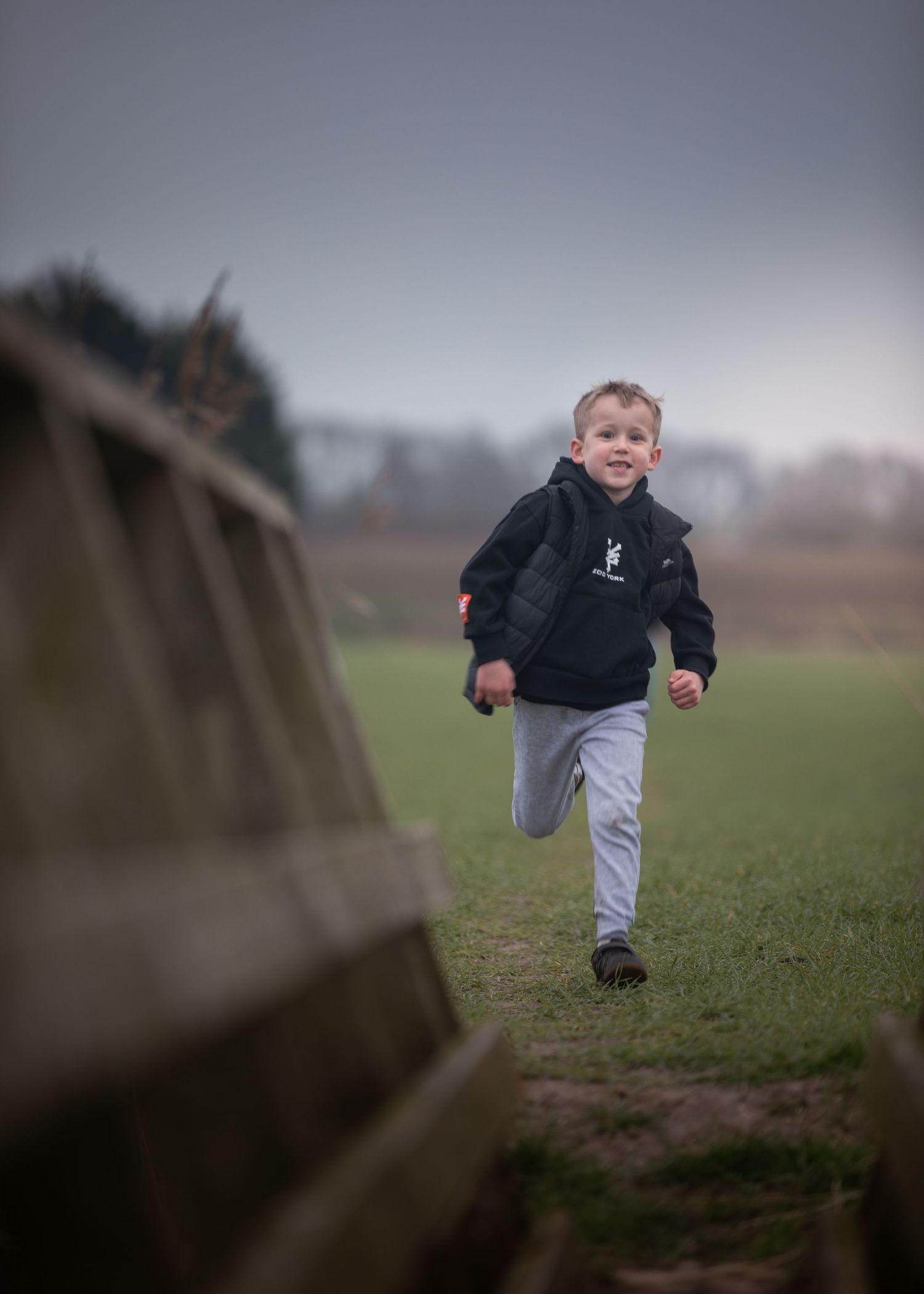 Happy young boy running across green field wearing black hoodie on overcast winter day outdoors.

Keyingham