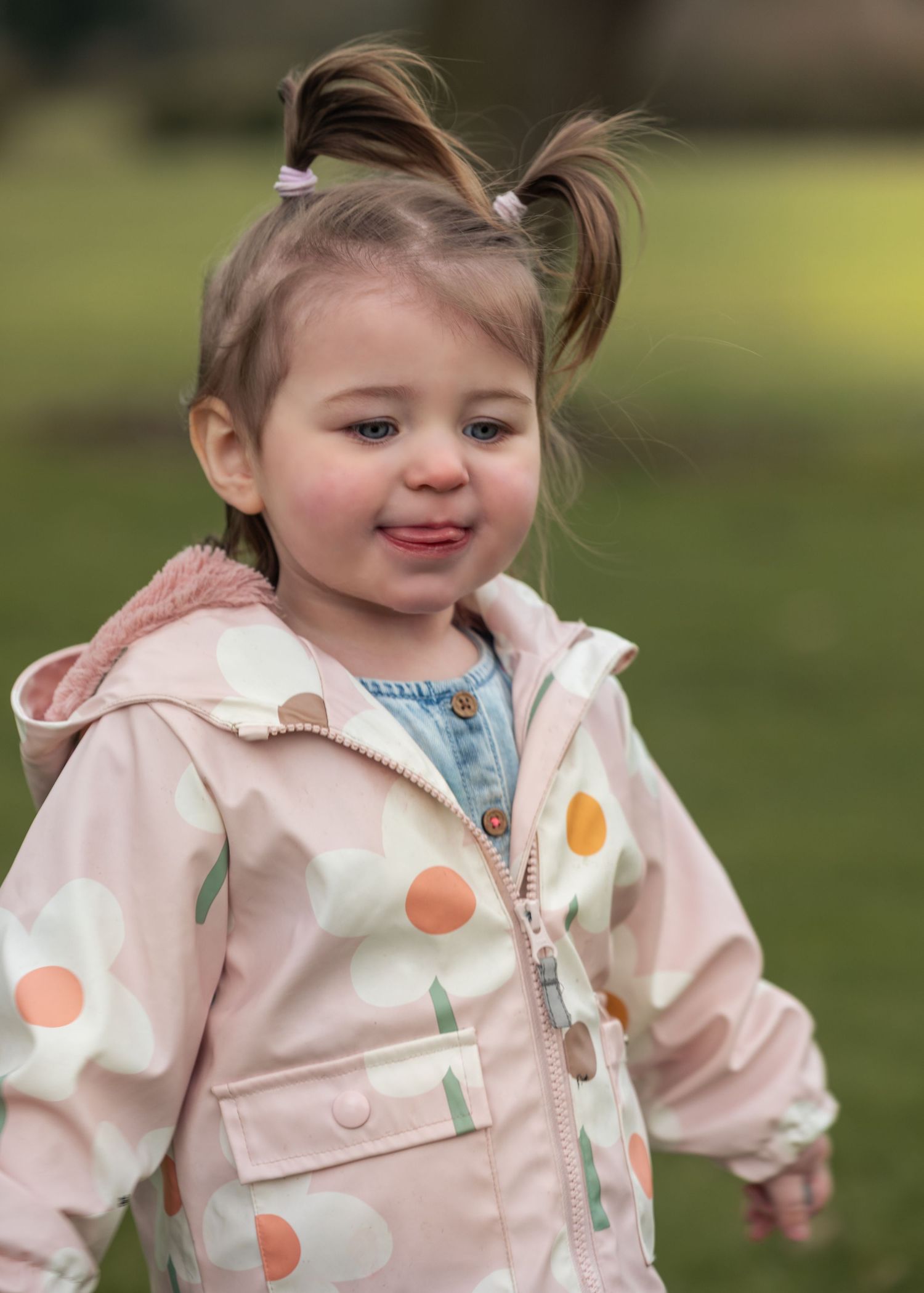 Cute toddler girl with pigtails wearing a floral pink jacket outdoors.