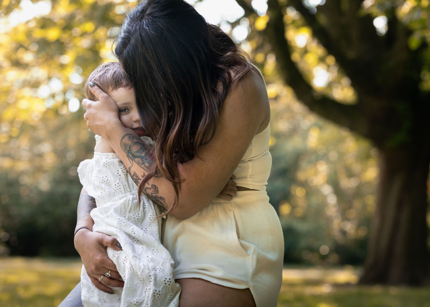 Tattooed mother tenderly embracing her baby child in autumn park with golden trees in background.

East Park Hull