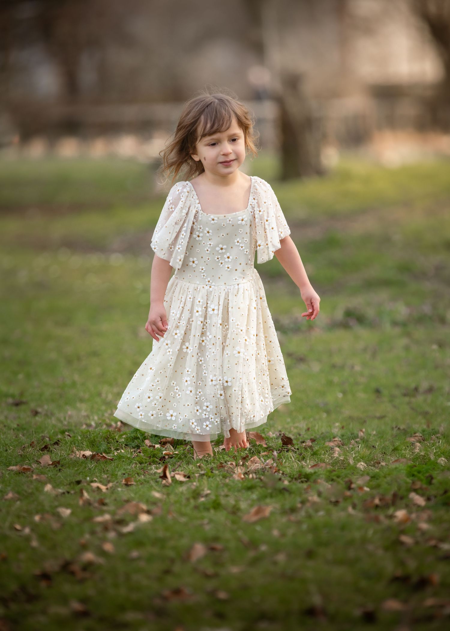 Smiling toddler girl in white floral eyelet dress walking barefoot on green grass.
East Park Hull
