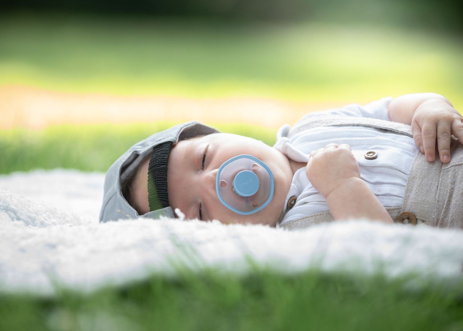 A peaceful baby sleeps on a white blanket in the grass with a blue pacifier on a sunny day.

East Park Hull