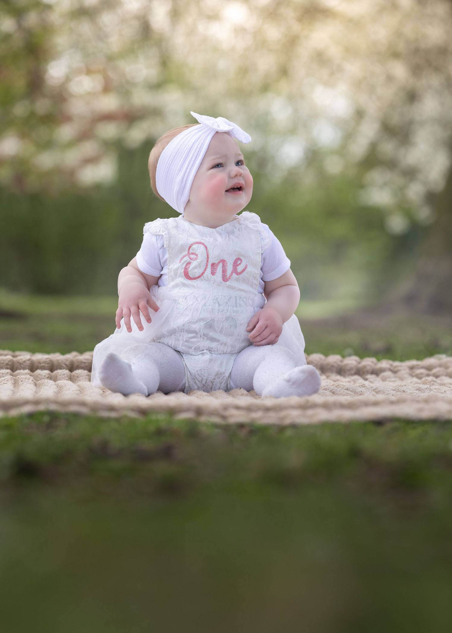 Baby girl in white lace romper with One embroidery sitting on blanket outdoors at golden hour.

East Park Hull