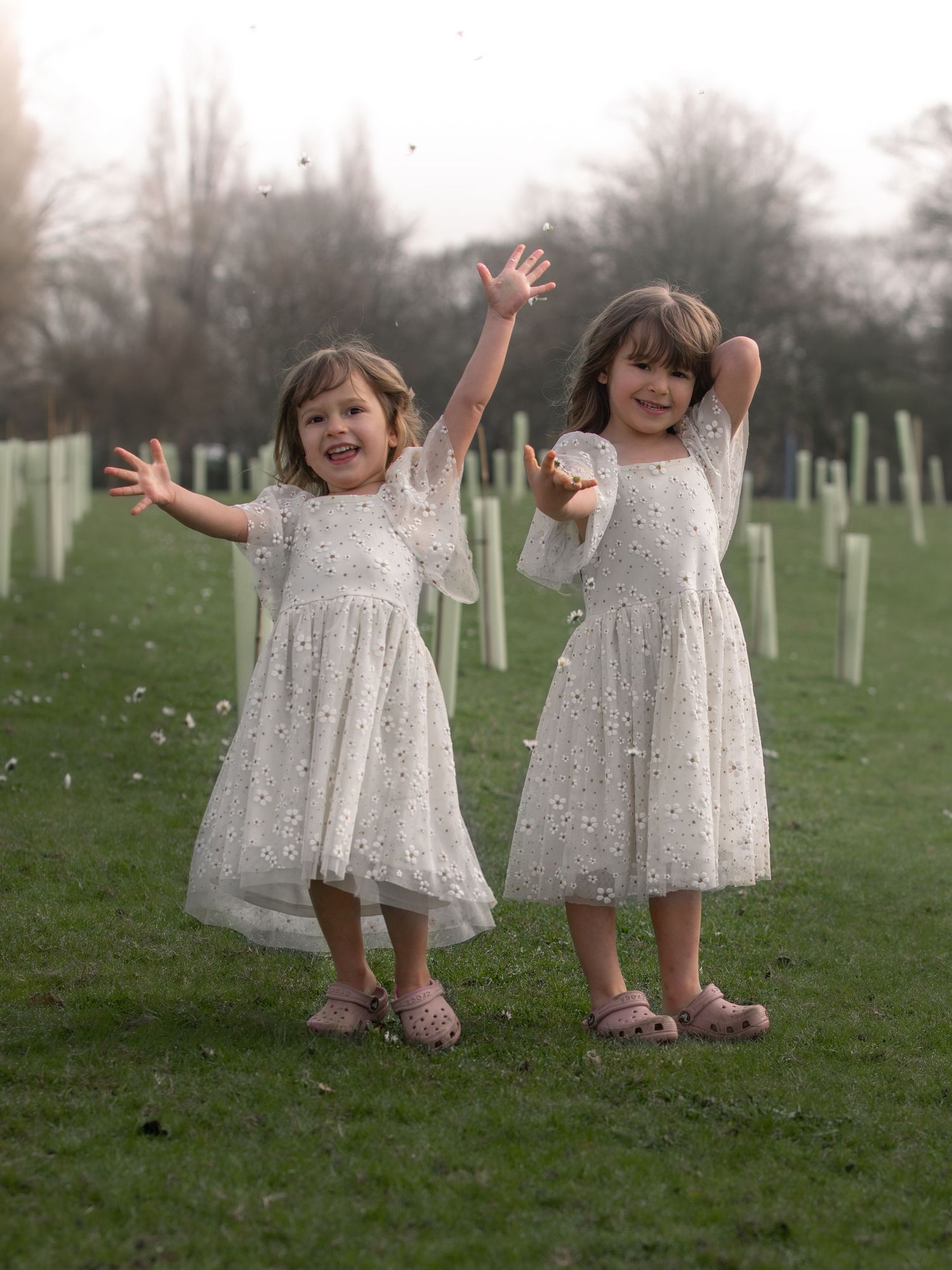 Two young girls in white floral dresses joyfully dancing outdoors in a green field.

East Park Hull