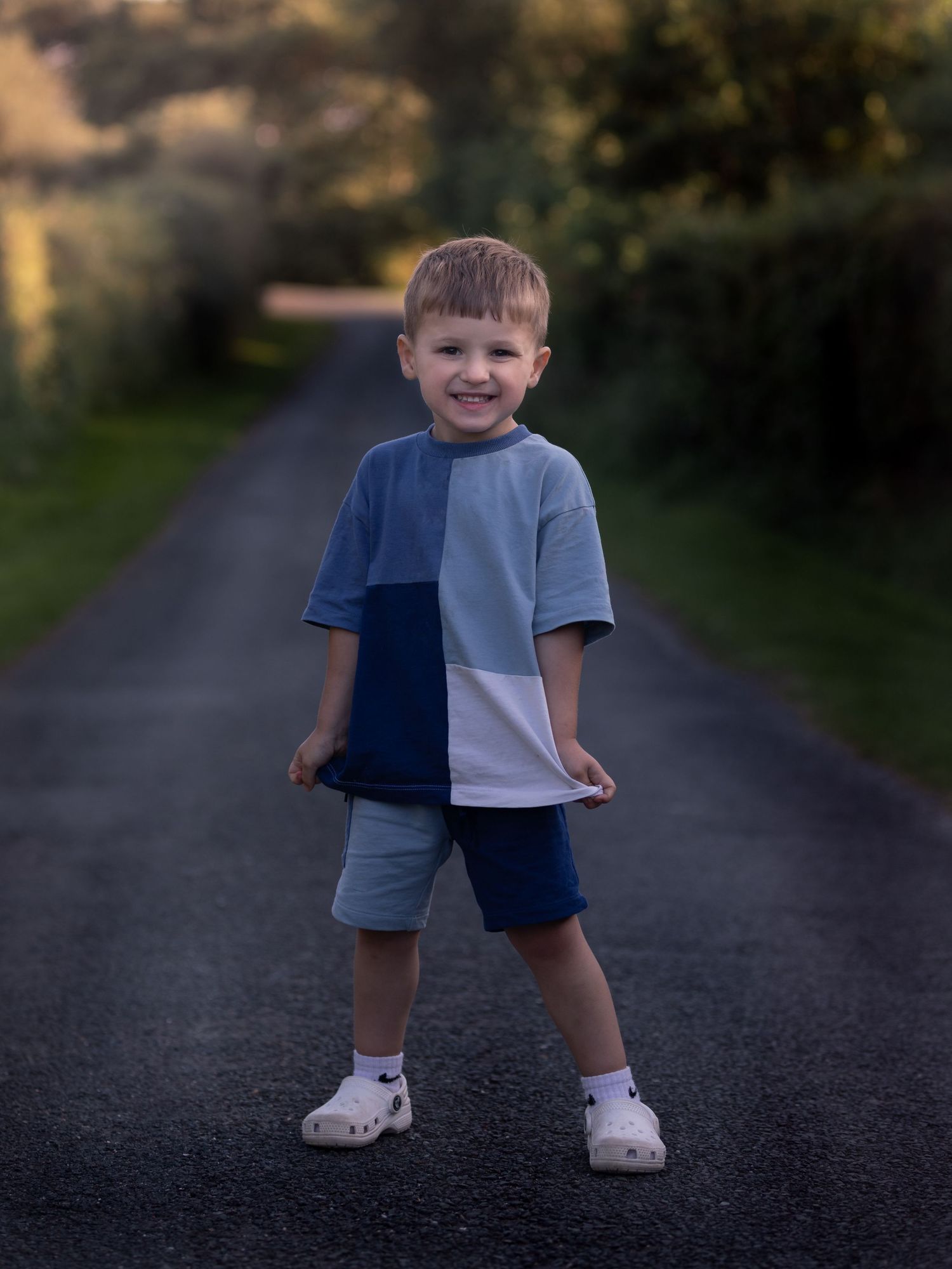 Smiling young boy in a blue color-block t-shirt standing on a country road.