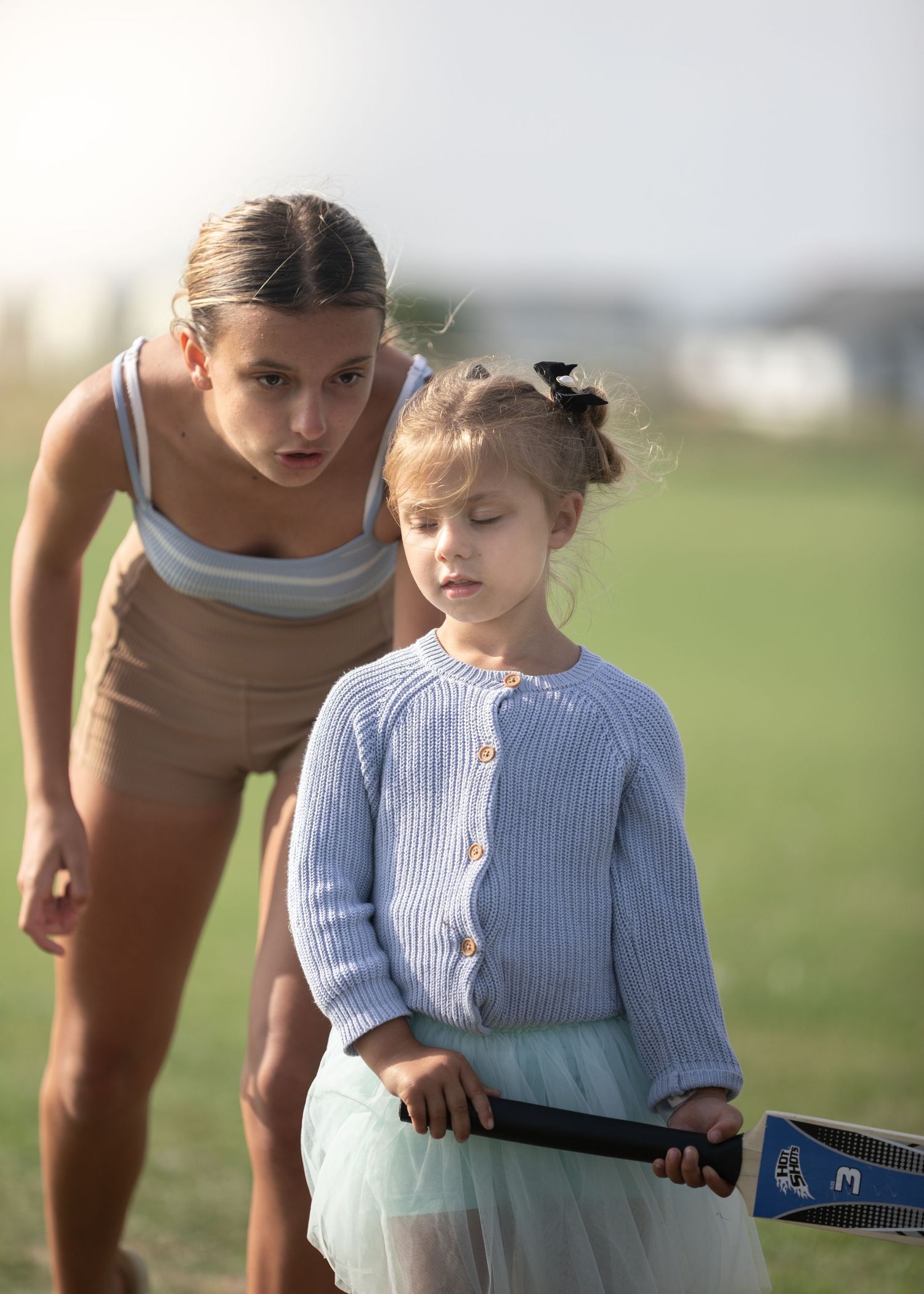 Older girl helps young child hold a badminton racket on a sunny outdoor field.

Blue Dolphin North Yorkshire