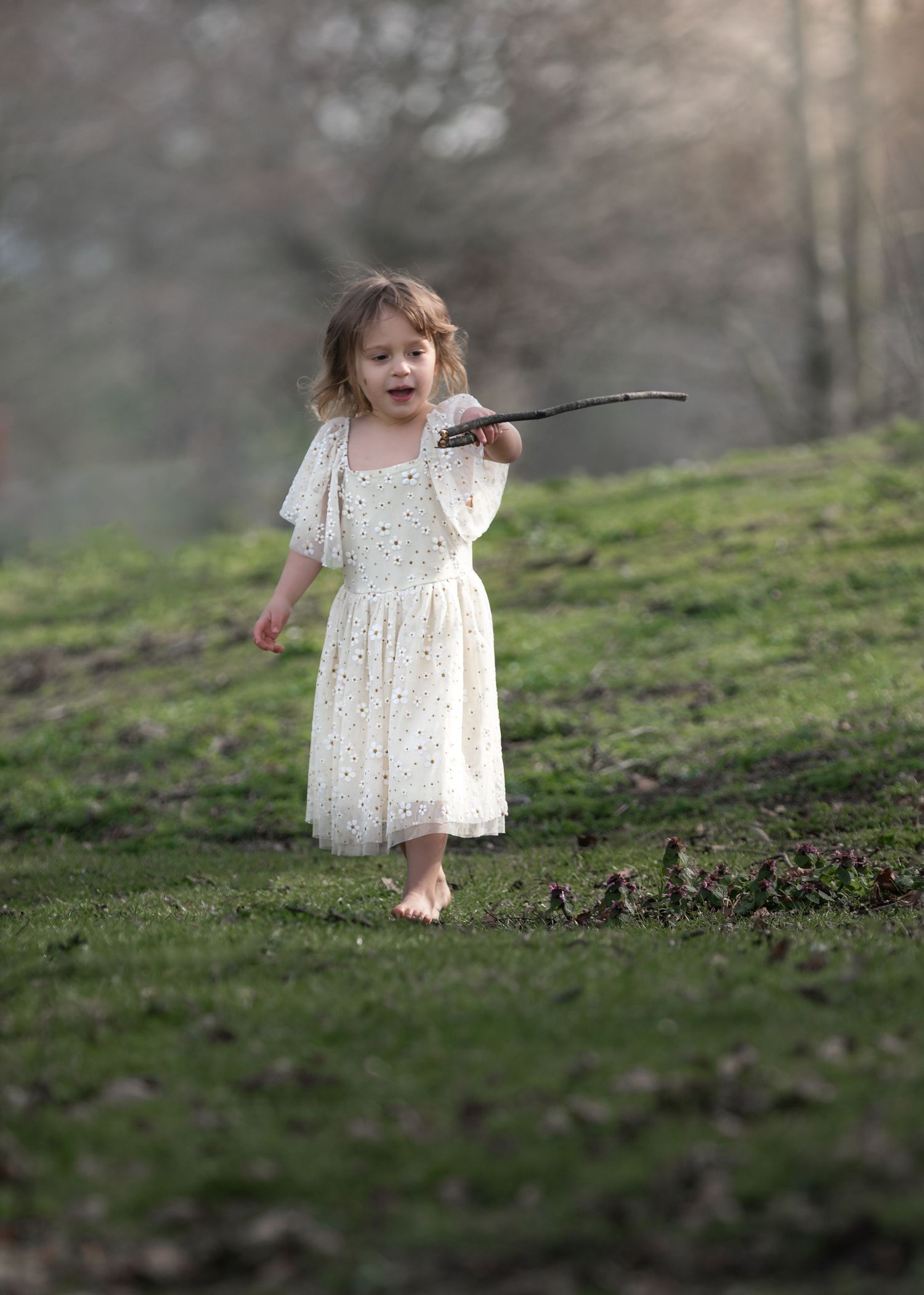 Barefoot toddler girl in white dress runs across grass holding a stick in a park.

East Park Hull