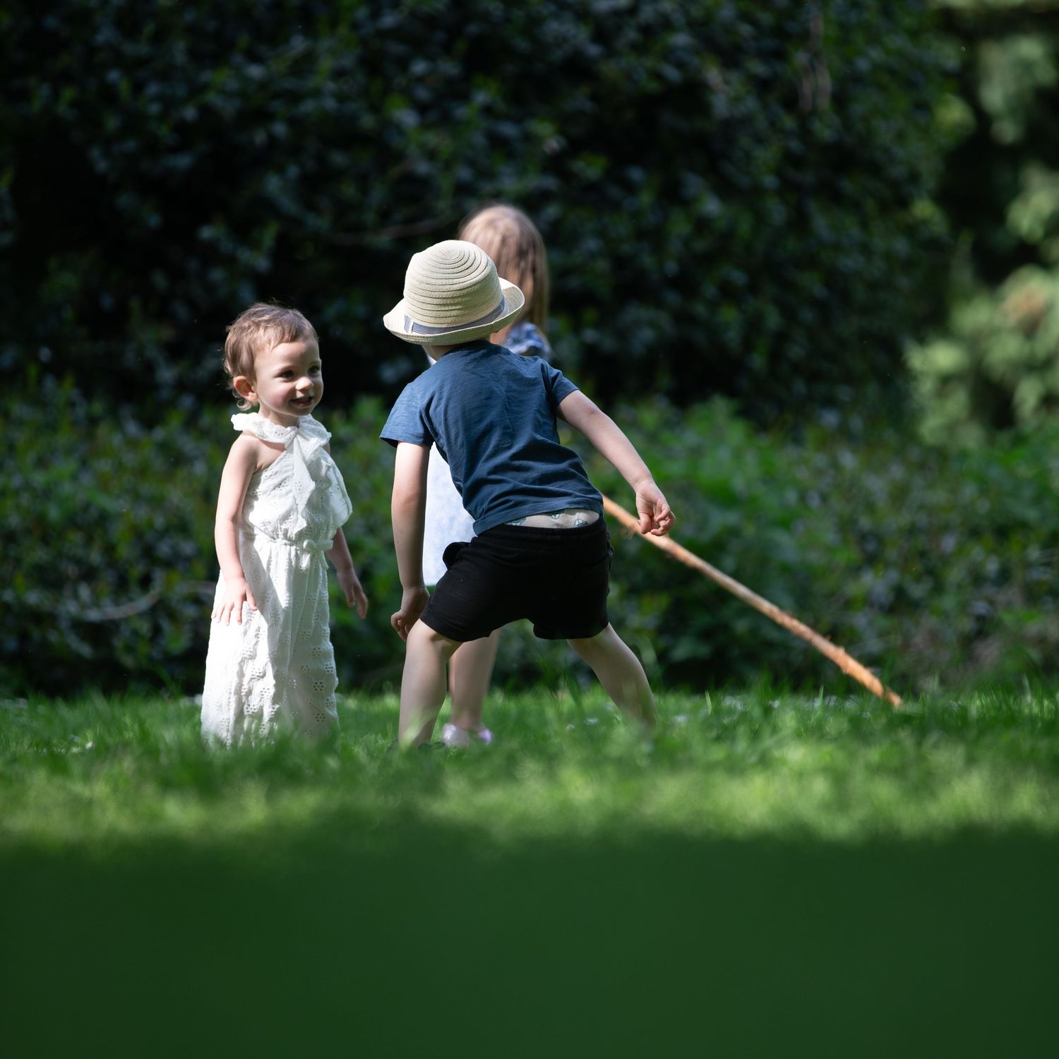 Two young children playing outdoors on a sunny green lawn with a stick.

East Park Hull