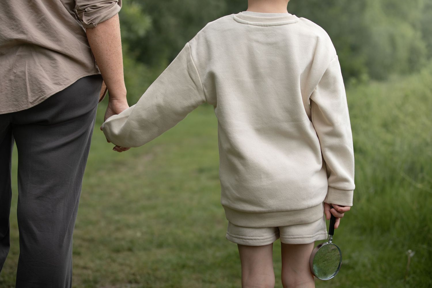 Adult and child walking hand in hand outdoors, child holding a magnifying glass, wearing matching cream sweatshirts.

Sutton Village