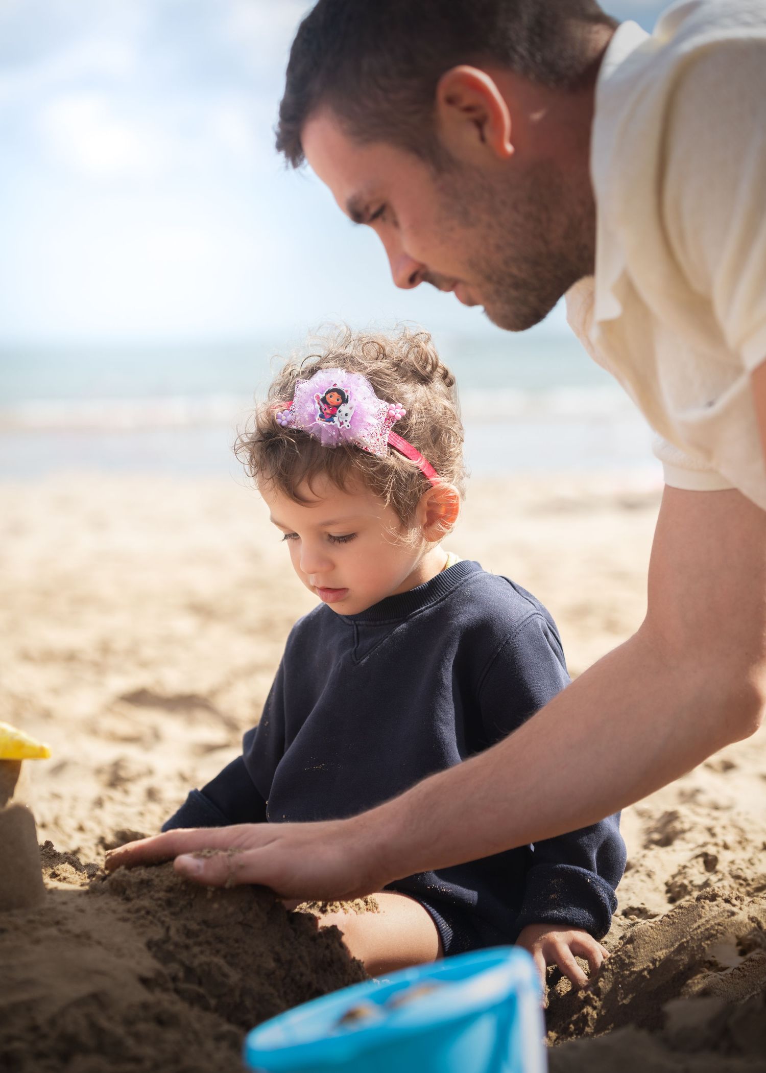 Father and toddler girl building sandcastles together on a sunny beach.

Scarborough