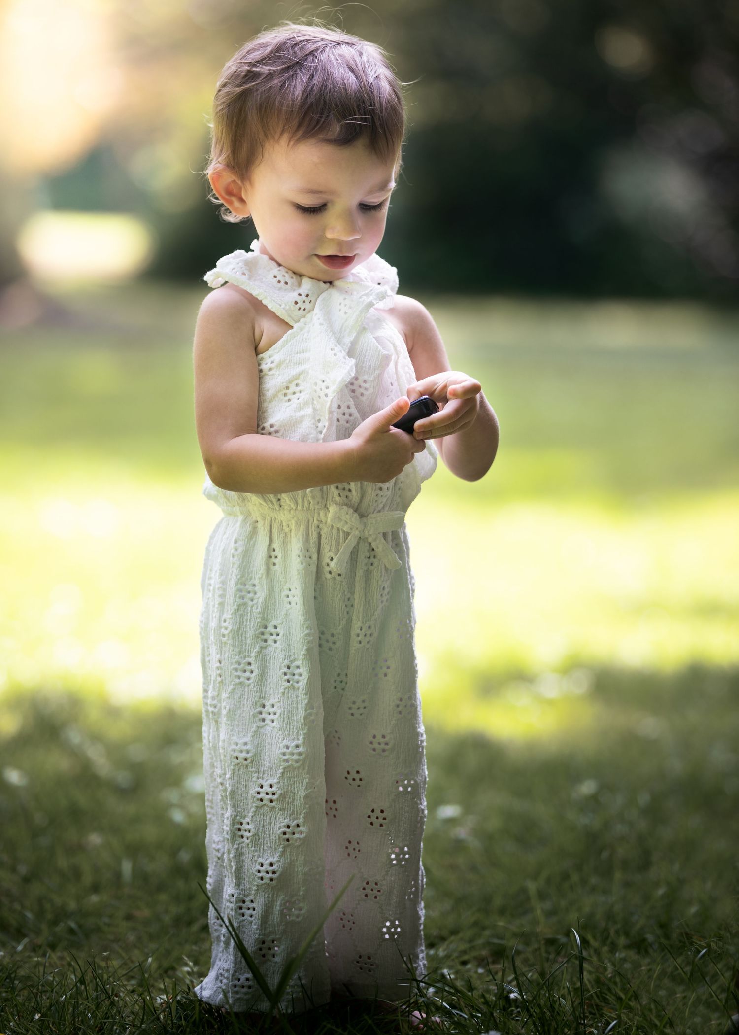 Toddler in a white eyelet dress standing on grass examining something small.

East Park Hull