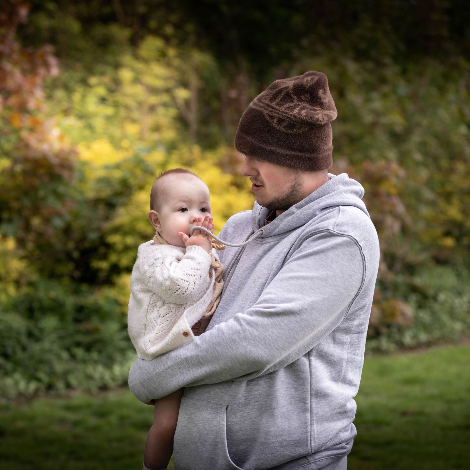 Father in grey hoodie and brown beanie tenderly holding his baby in a lush green garden setting.

East Park Hull