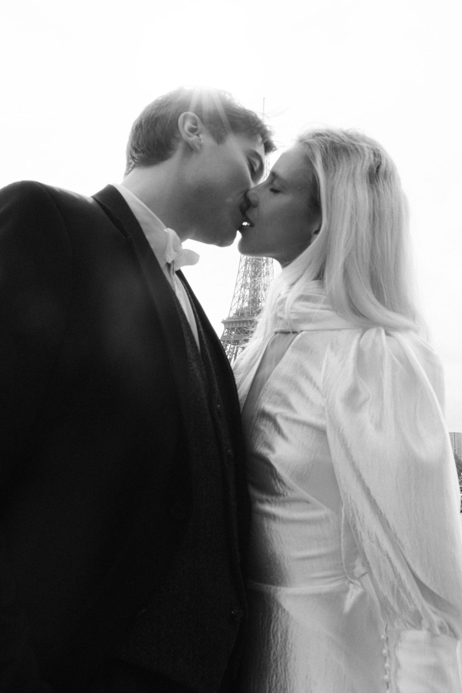 Bride and groom share a romantic kiss with the iconic Eiffel Tower visible in soft background.