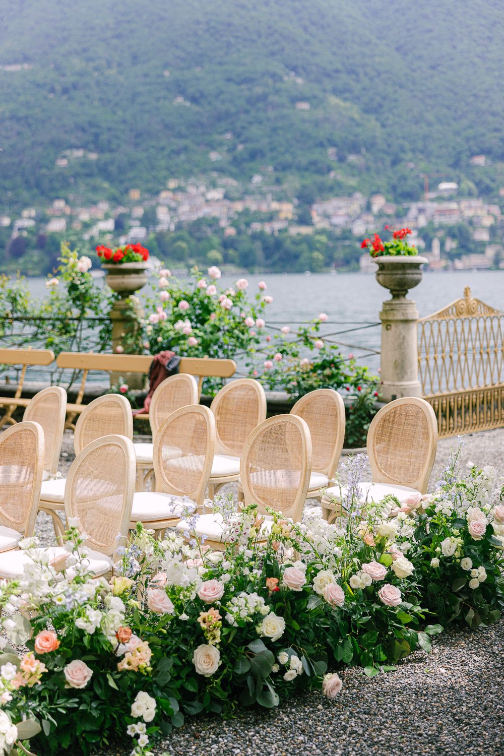 Romantic outdoor wedding ceremony setup with rattan chairs lined with lush floral arrangements overlooking Lake Como.