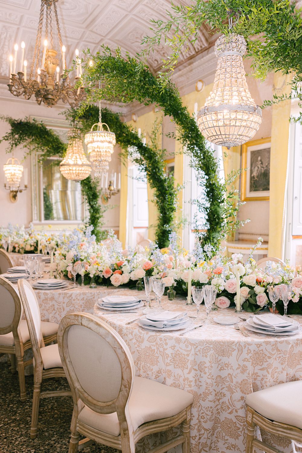 Elegant wedding reception with greenery arch, crystal chandeliers, and blush floral centerpieces.