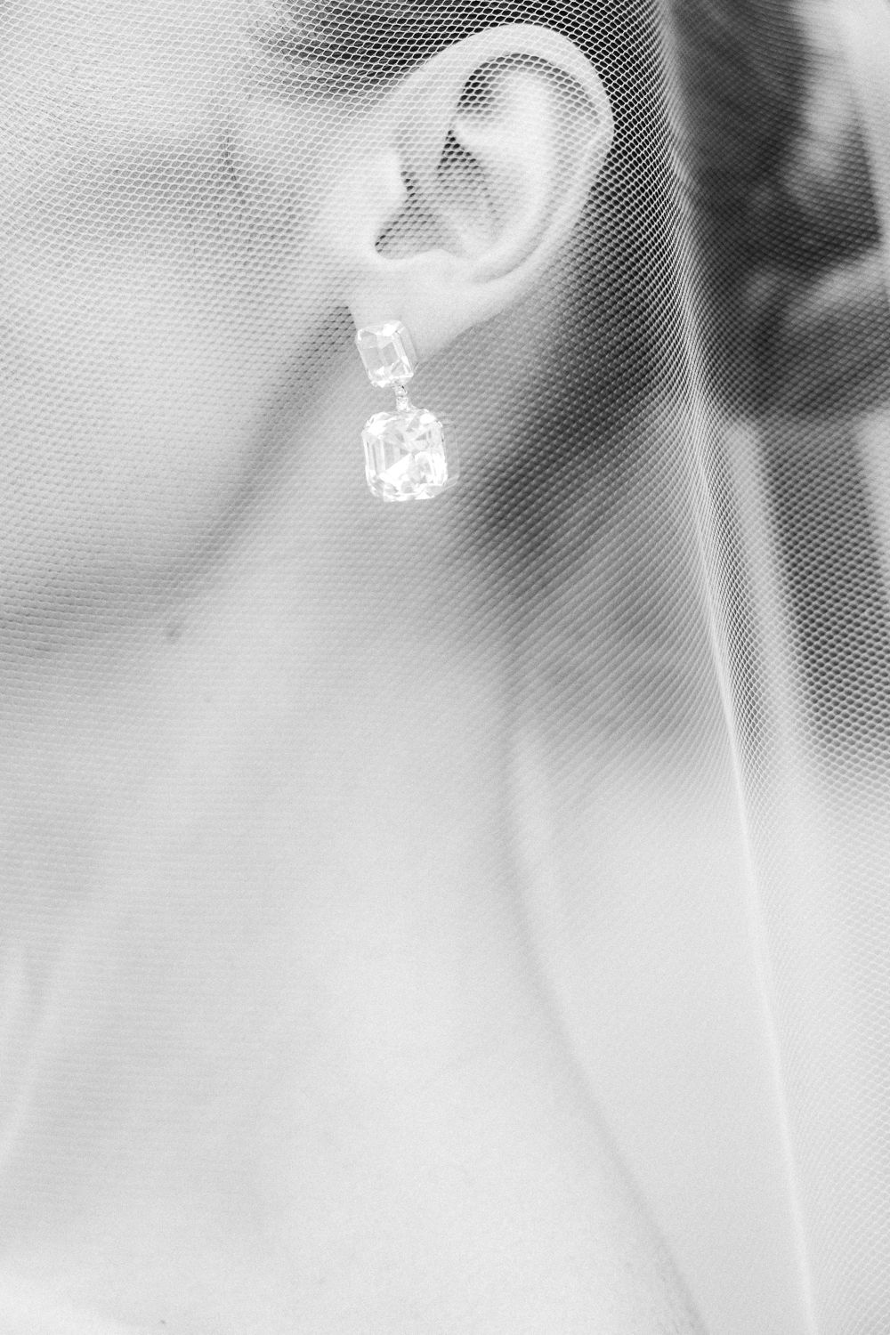 Close-up of bride wearing elegant diamond drop earring partially veiled in soft white tulle fabric.