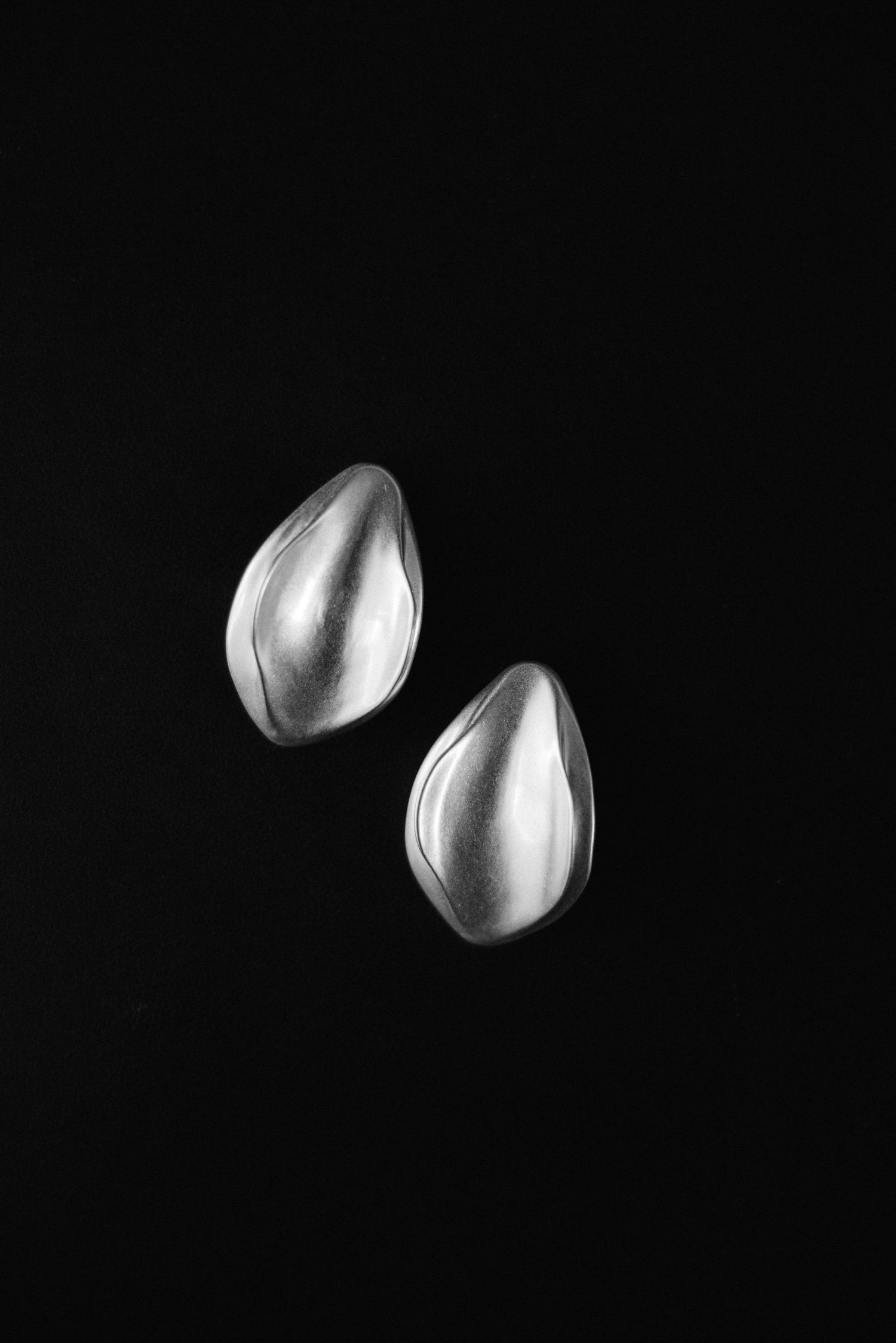 Black and white product photo of two silver teardrop-shaped earrings on dark background.