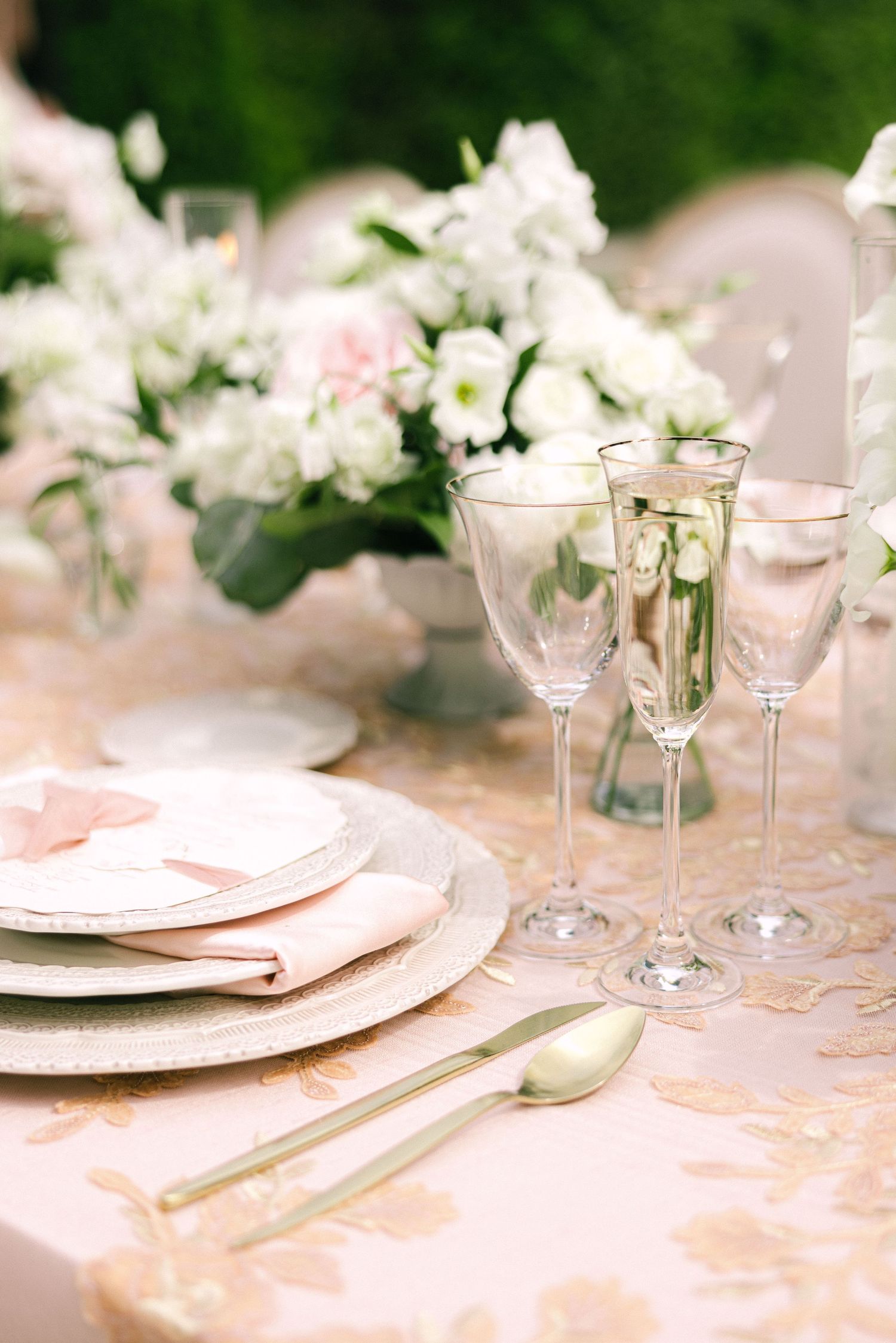 Elegant wedding table setting with crystal champagne flutes, gold cutlery, blush napkins, and white floral centerpieces.