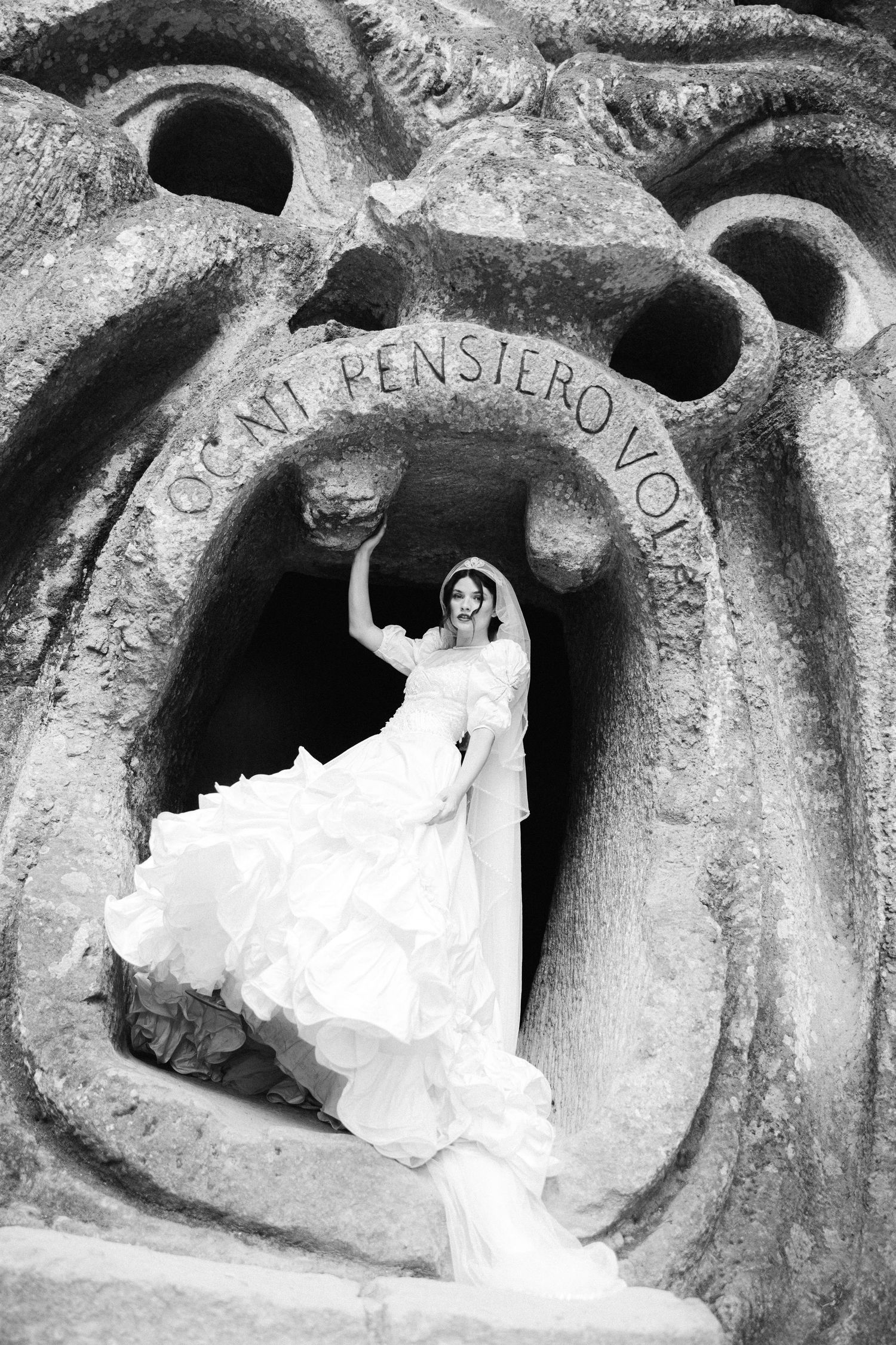 Bride in flowing white gown posing inside the famous monster mouth sculpture at Bomarzo Garden of Monsters, Italy.